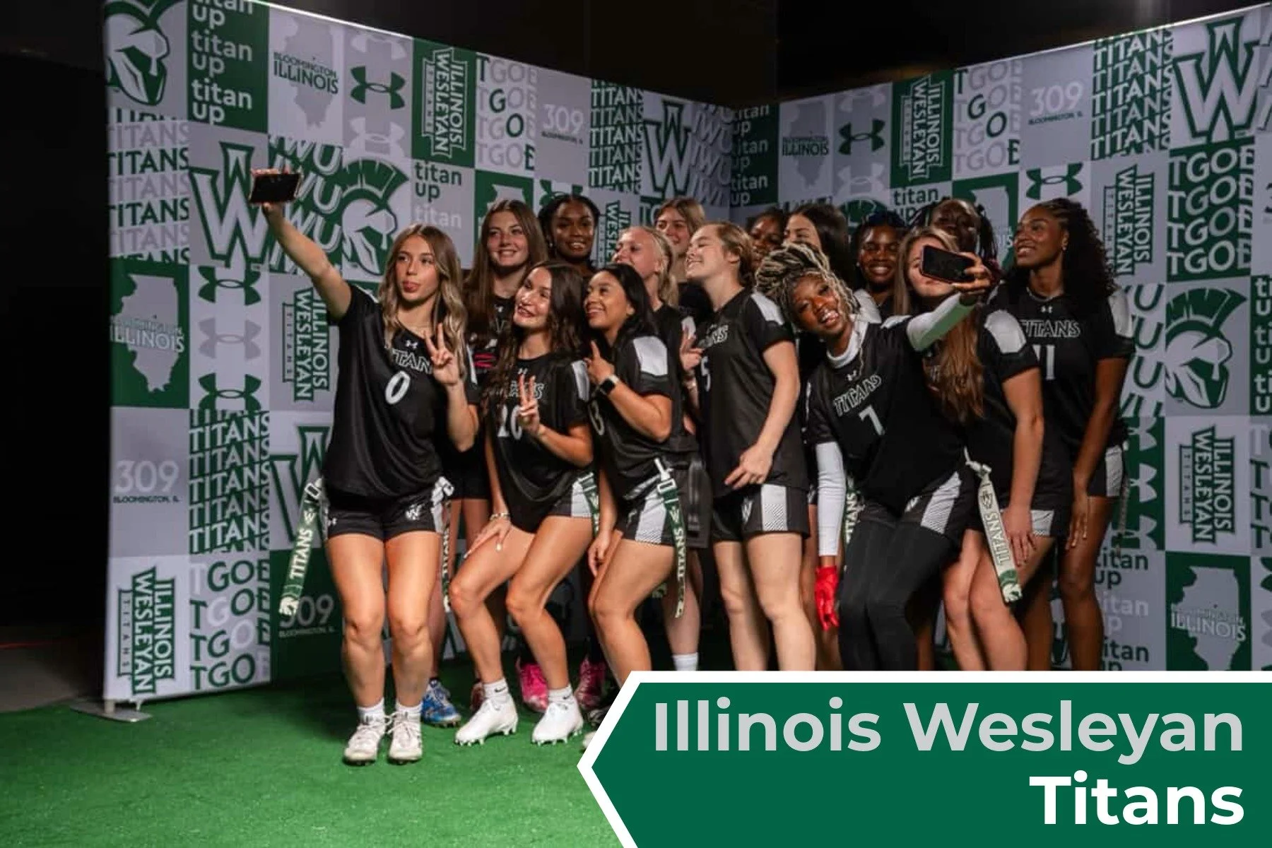 Group of female athletes wearing black uniforms with white accents, taking a selfie in front of a backdrop with 'Illinois Wesleyan Titans' logos, and a green banner with the same name.