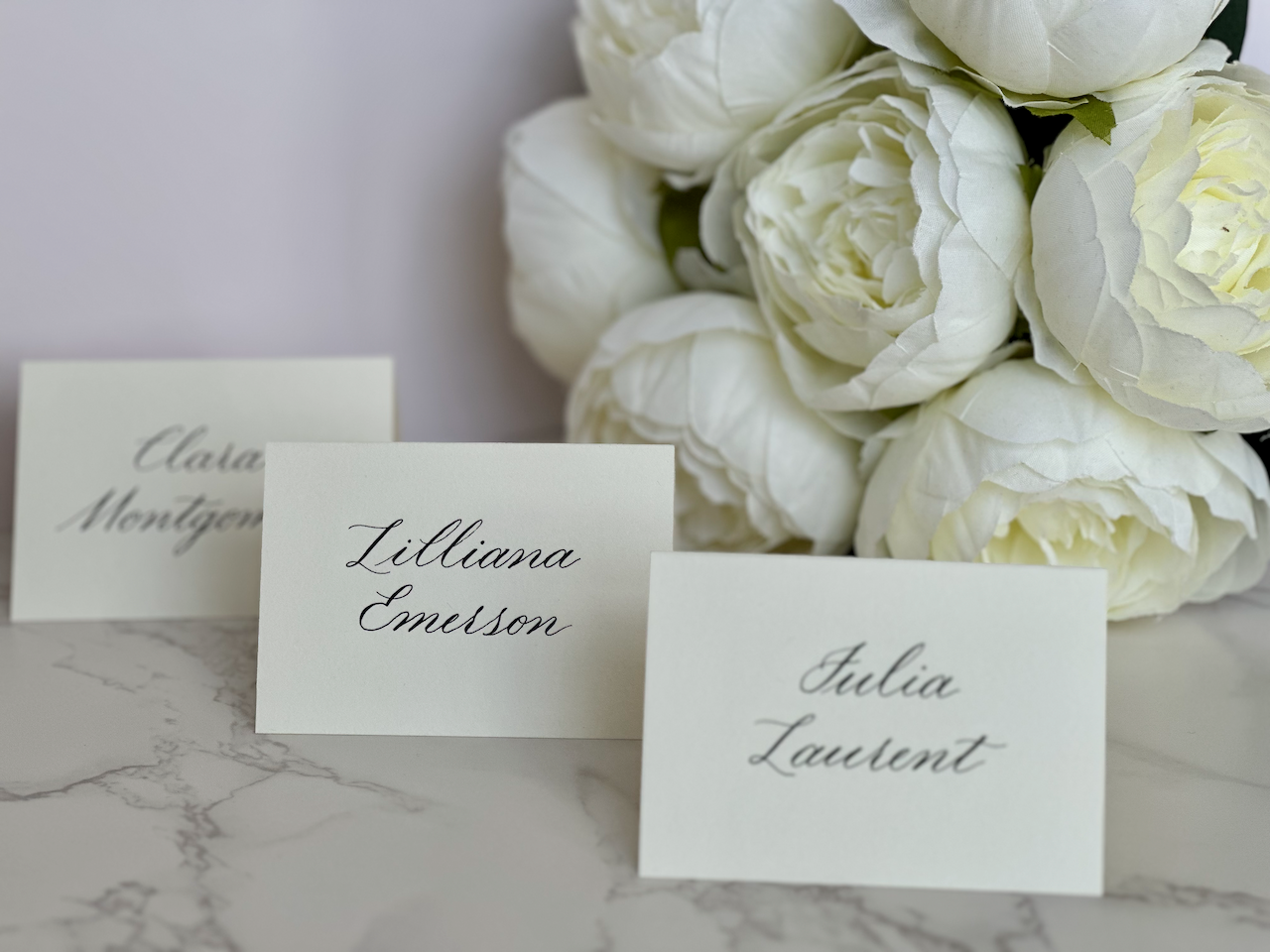 Set of custom hand-written calligraphy place cards for wedding guests on cream paper with floral decor