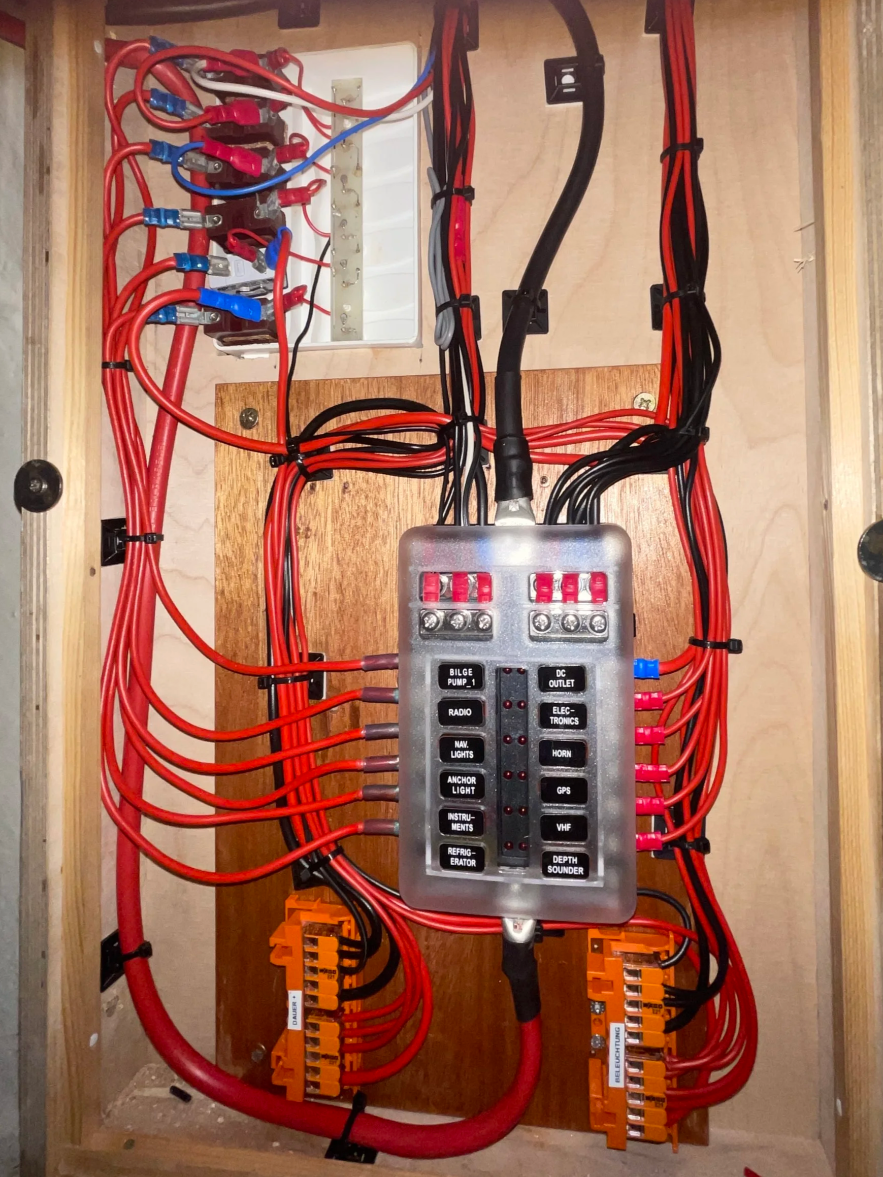 Elektrischer Schaltschrank mit roten und schwarzen Kabeln, einem Verteilungsboard und Kontrollschaltern, die auf einem Holzbrett befestigt sind.