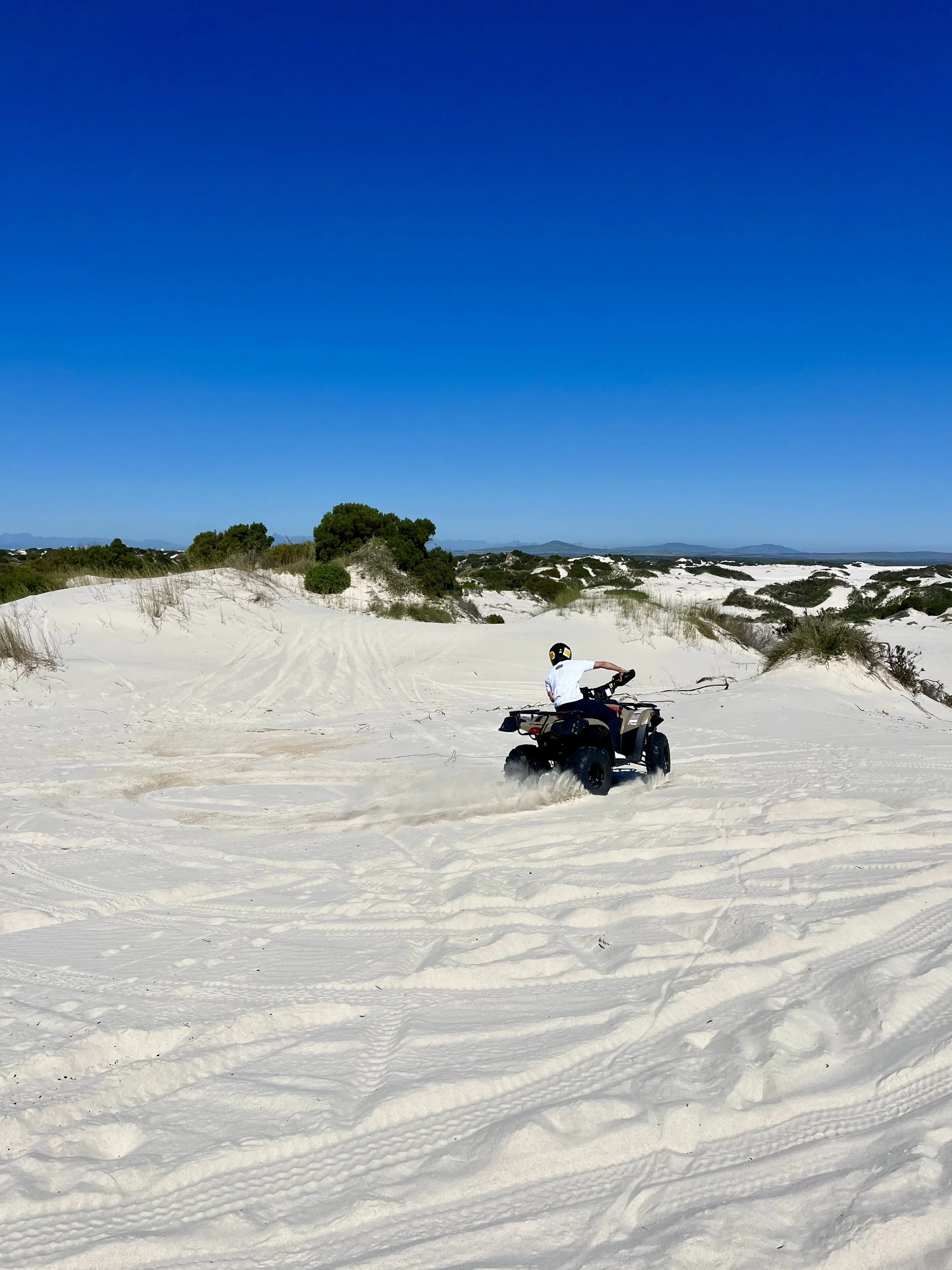 Person riding an ATV on sandy dunes under a clear blue sky