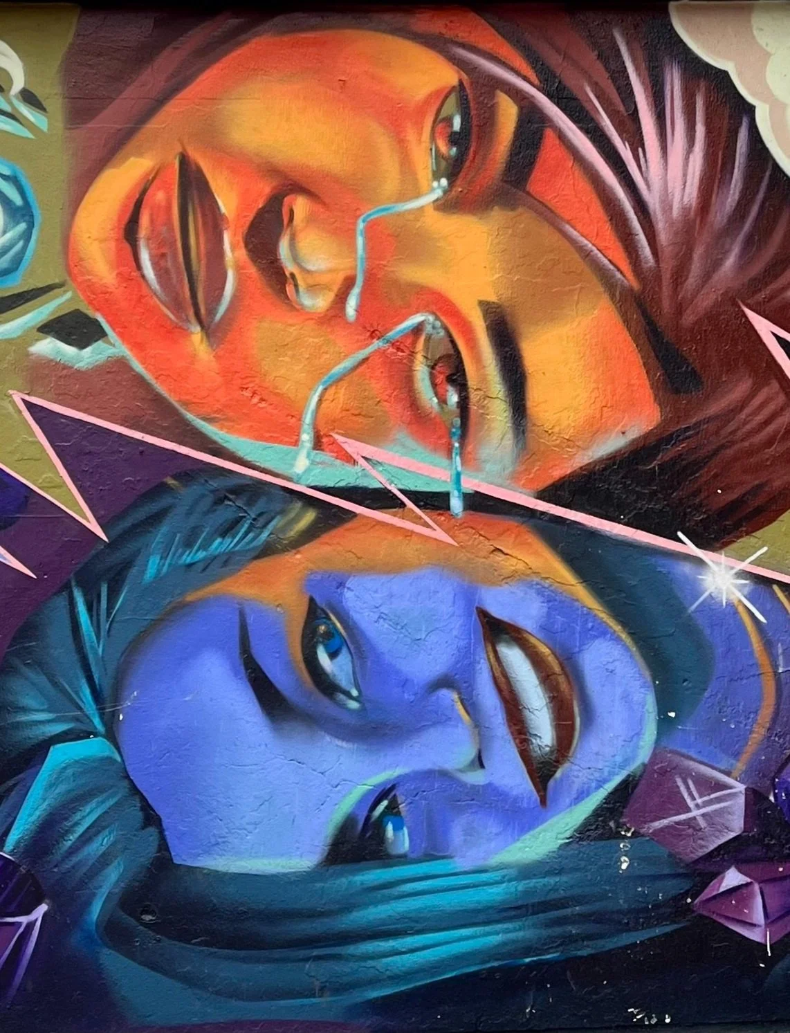 Colorful street art mural featuring two stylized faces with vibrant colors and geometric elements.