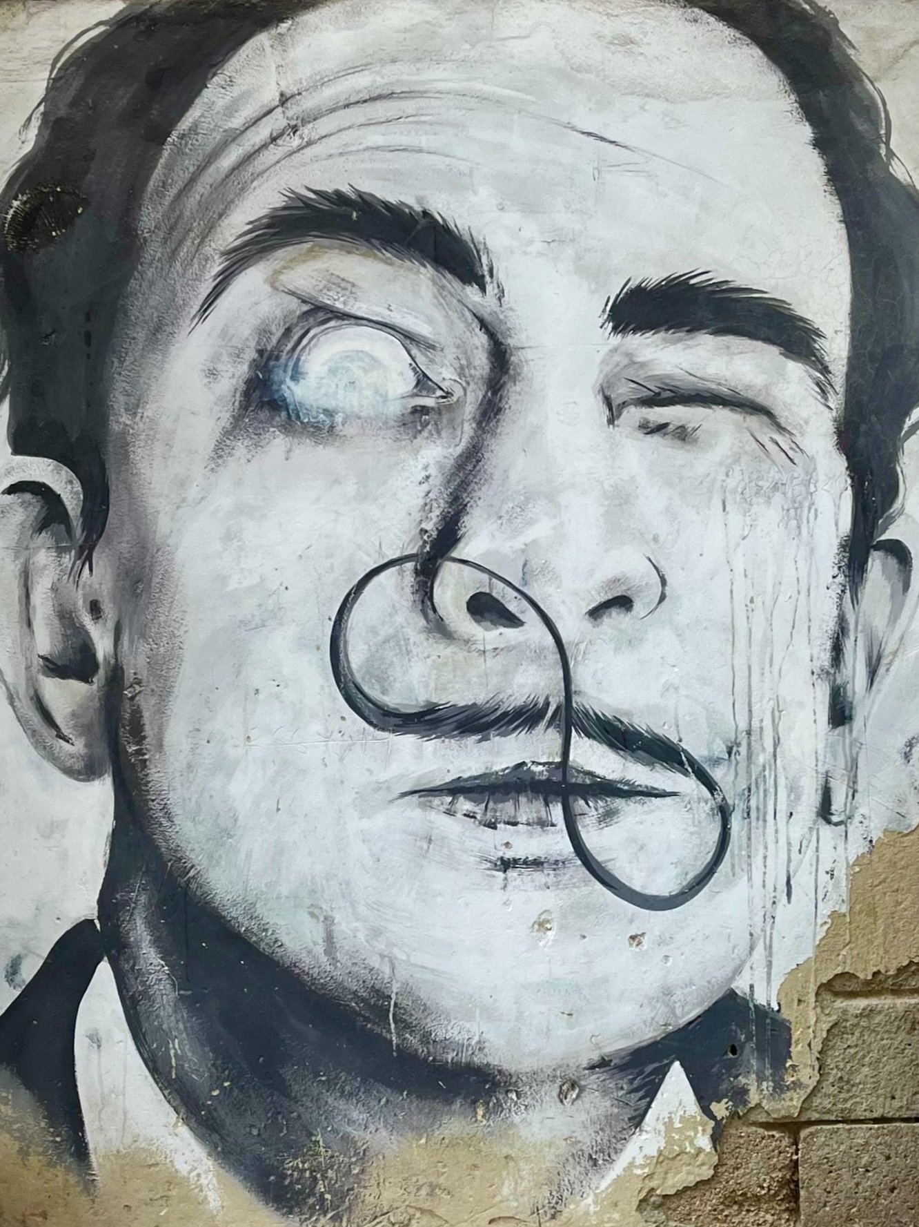Graffiti of a man with distinct facial features, including a curled mustache and expressive eyes, painted on a weathered wall.