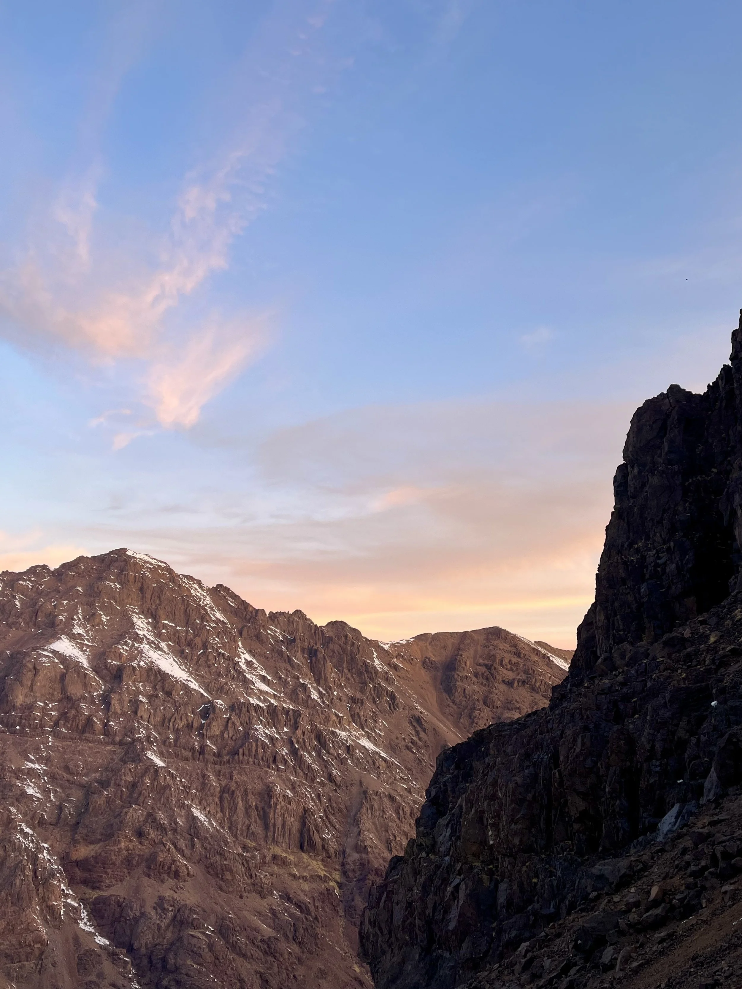 Rocky mountain landscape with snow patches under a clear blue sky at sunrise or sunset.