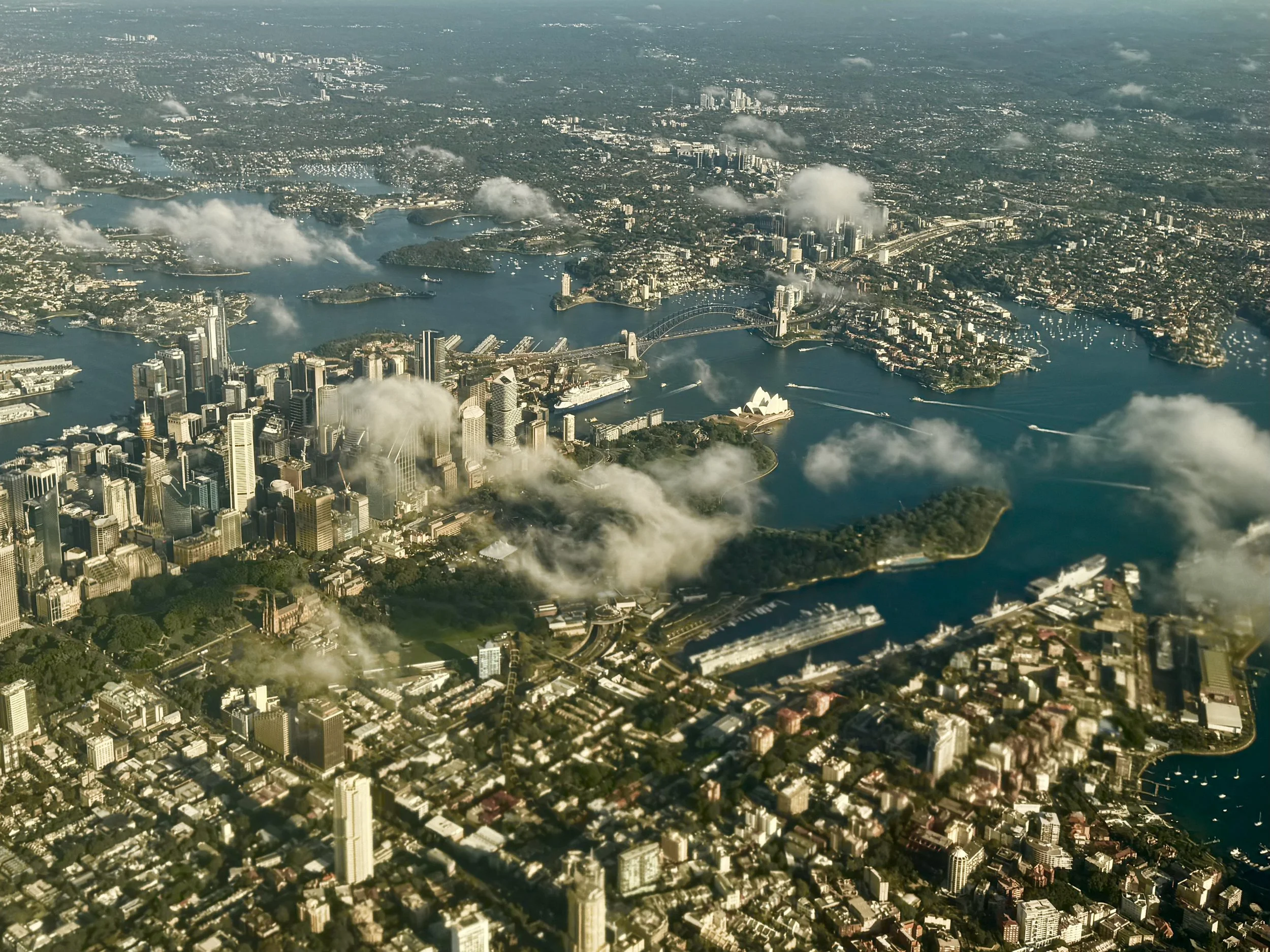 Aerial view of Sydney, Australia, featuring the Opera House, harbor, and cityscape with clouds scattered above.