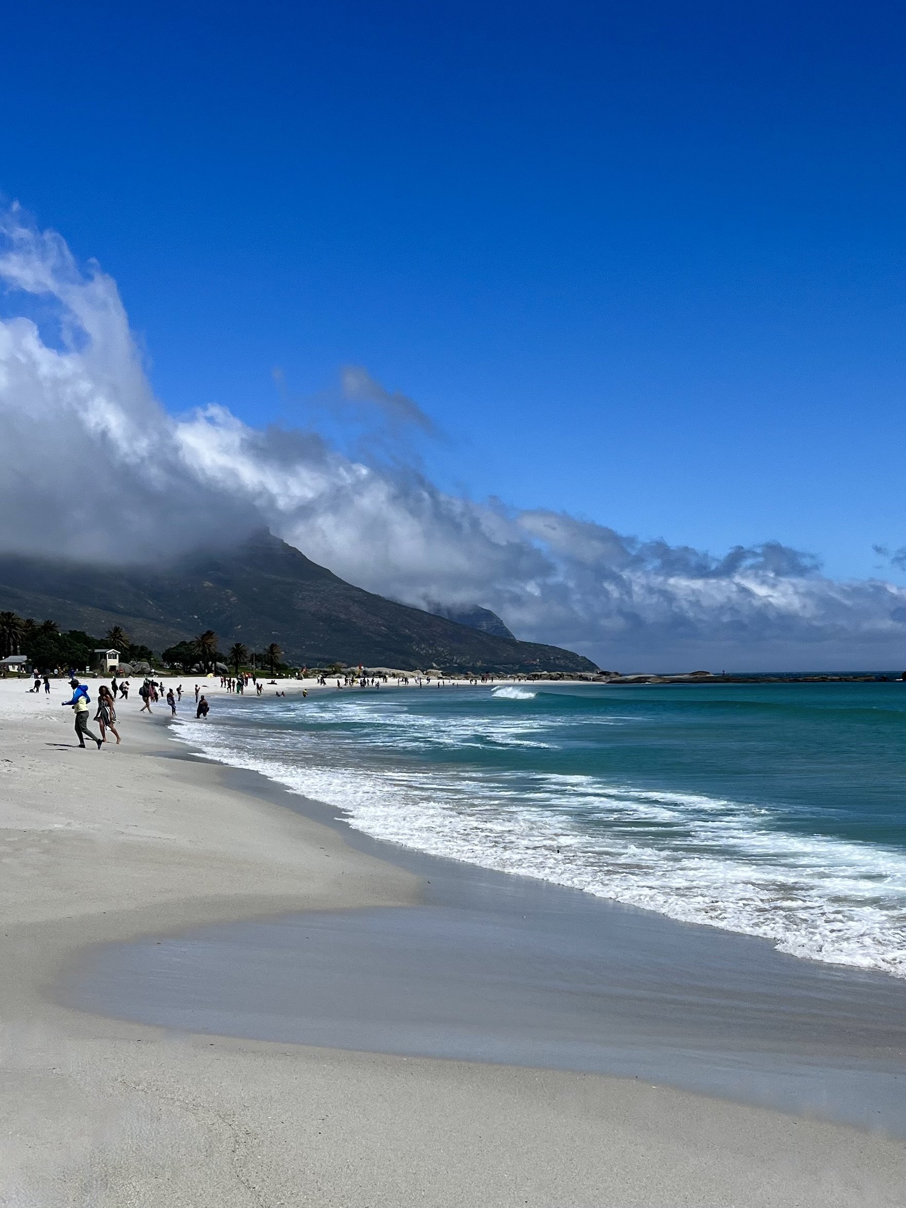 Sandy beach with waves and people, mountain and clouds in background