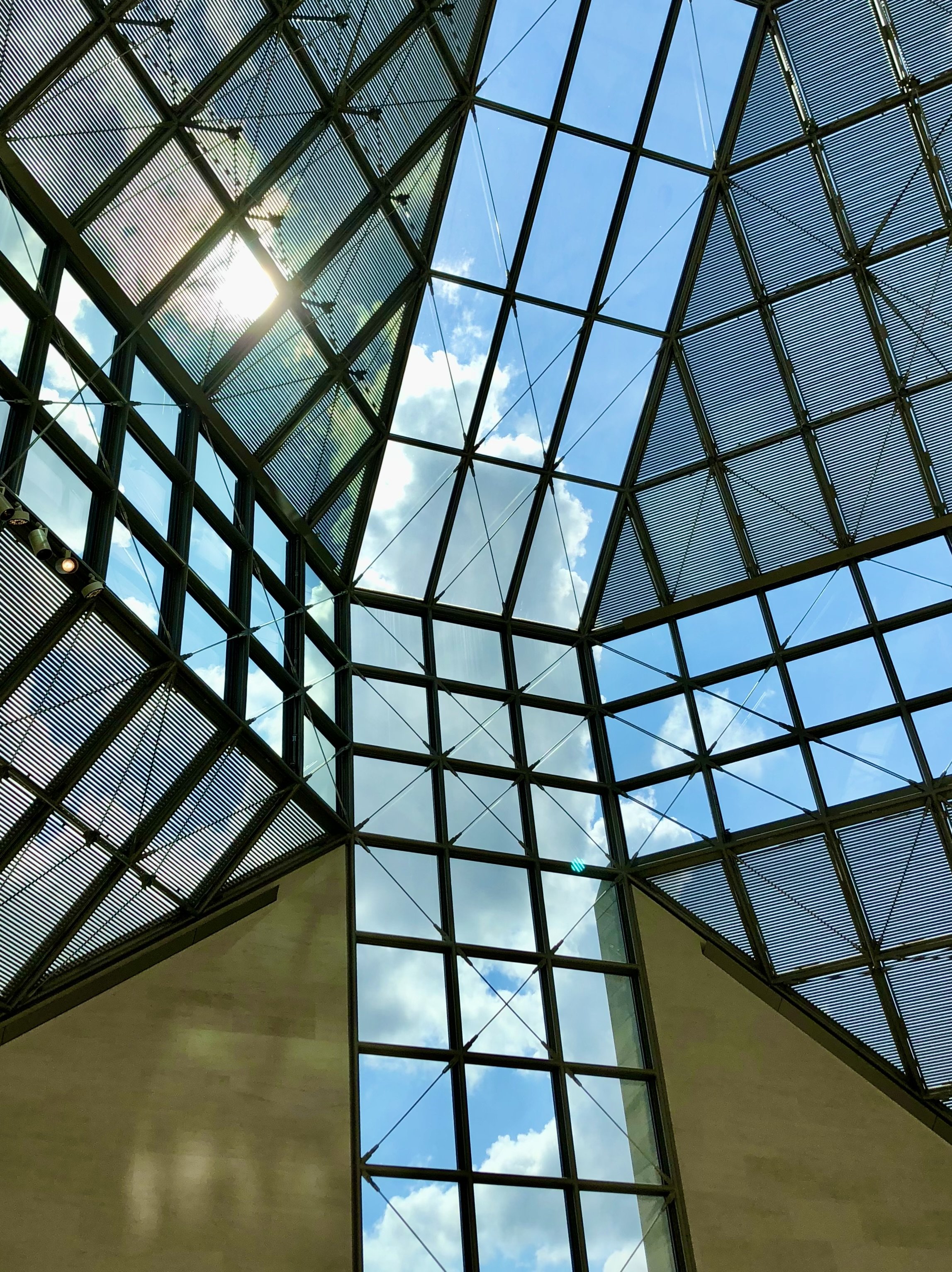 View of a blue sky with clouds through a modern glass ceiling structure.