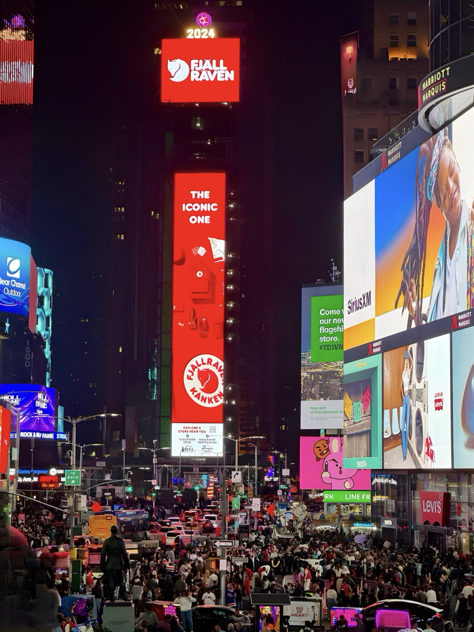 Times Square at night with crowds and bright electronic billboards, featuring ads for Fjällräven, Levi's, and other brands.