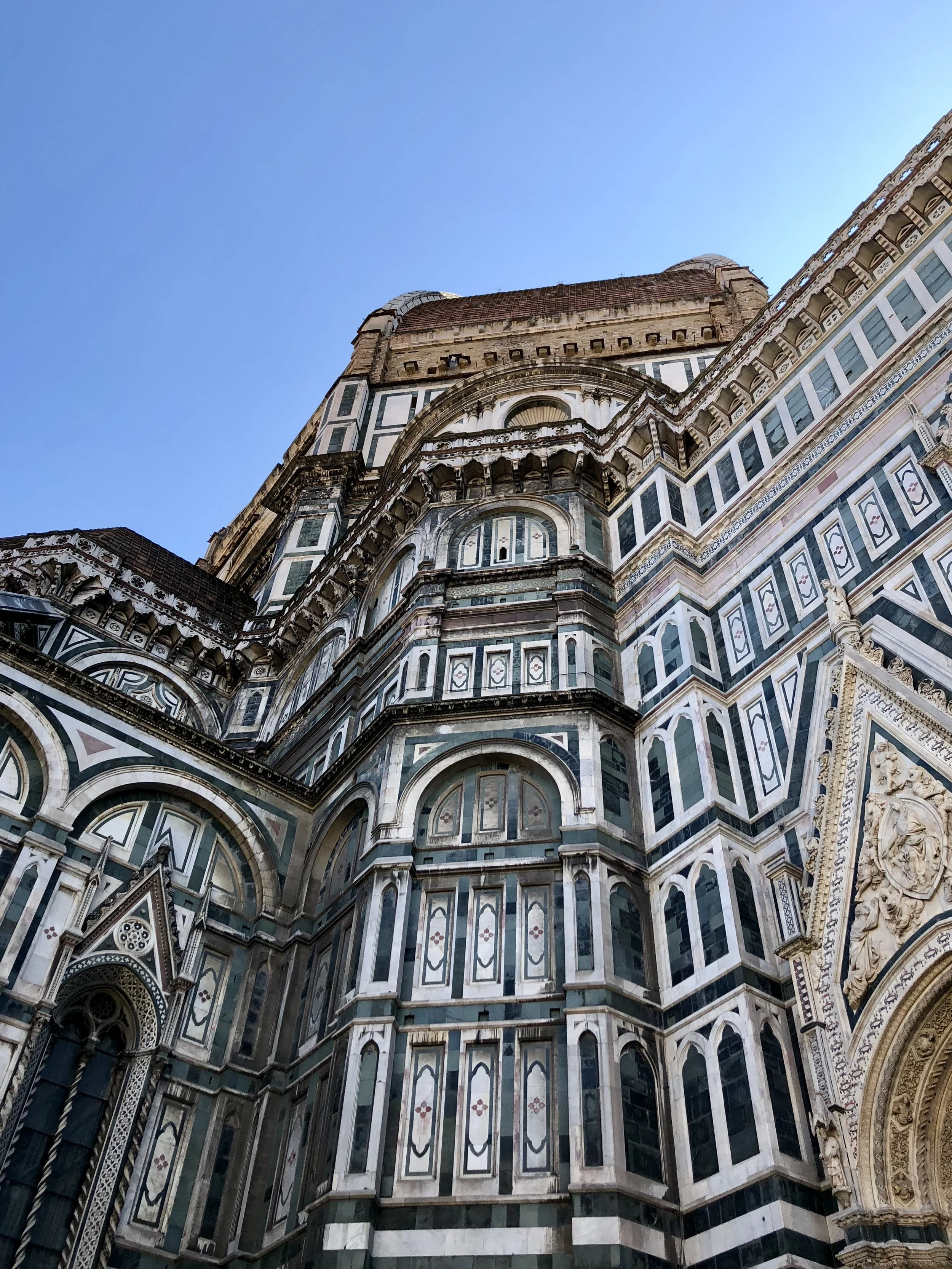 Close-up of the intricate facade of the Florence Cathedral, featuring ornate architectural details and marble paneling against a clear blue sky.