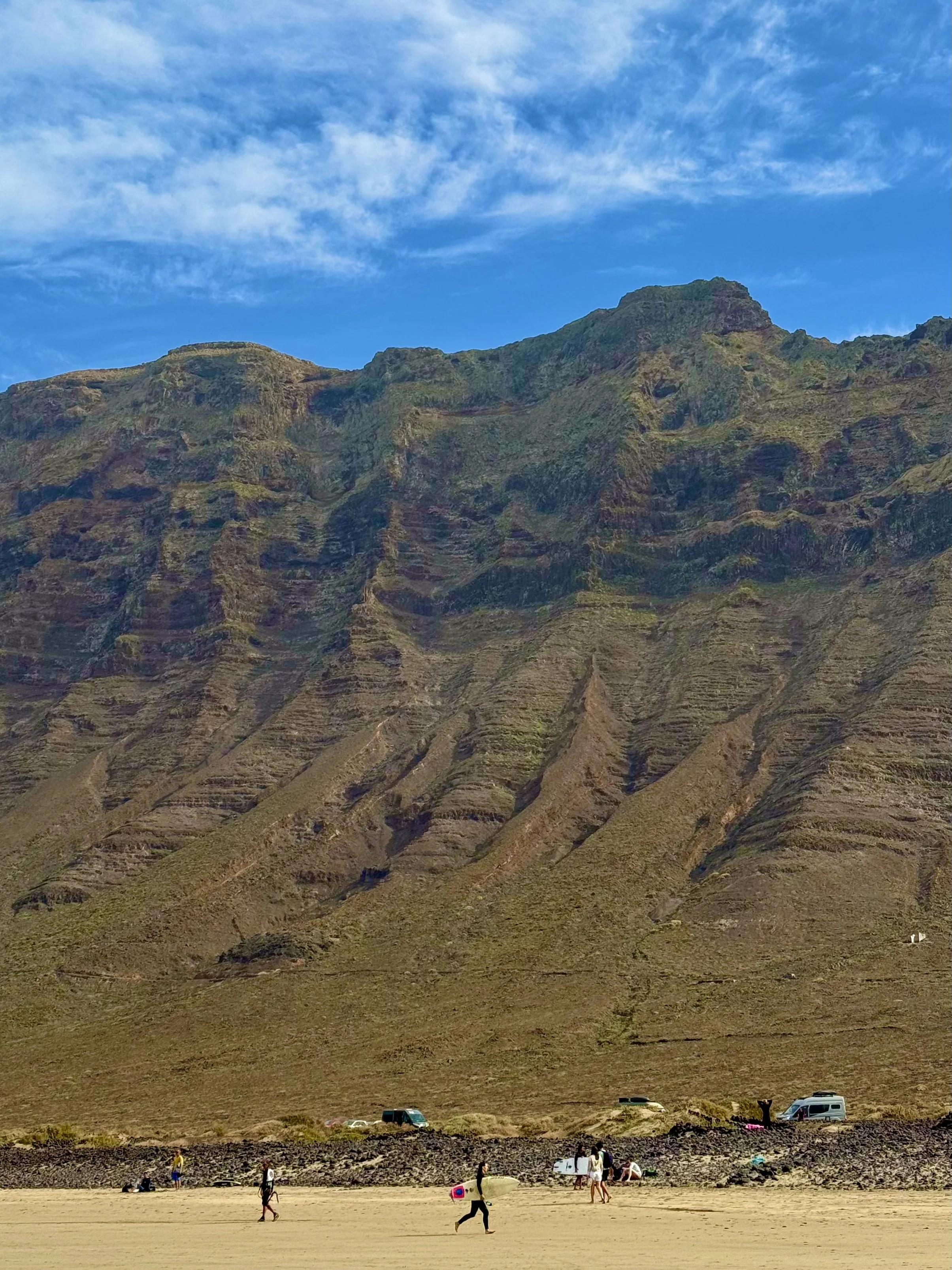 Beach with people playing in front of large cliff and cloudy sky