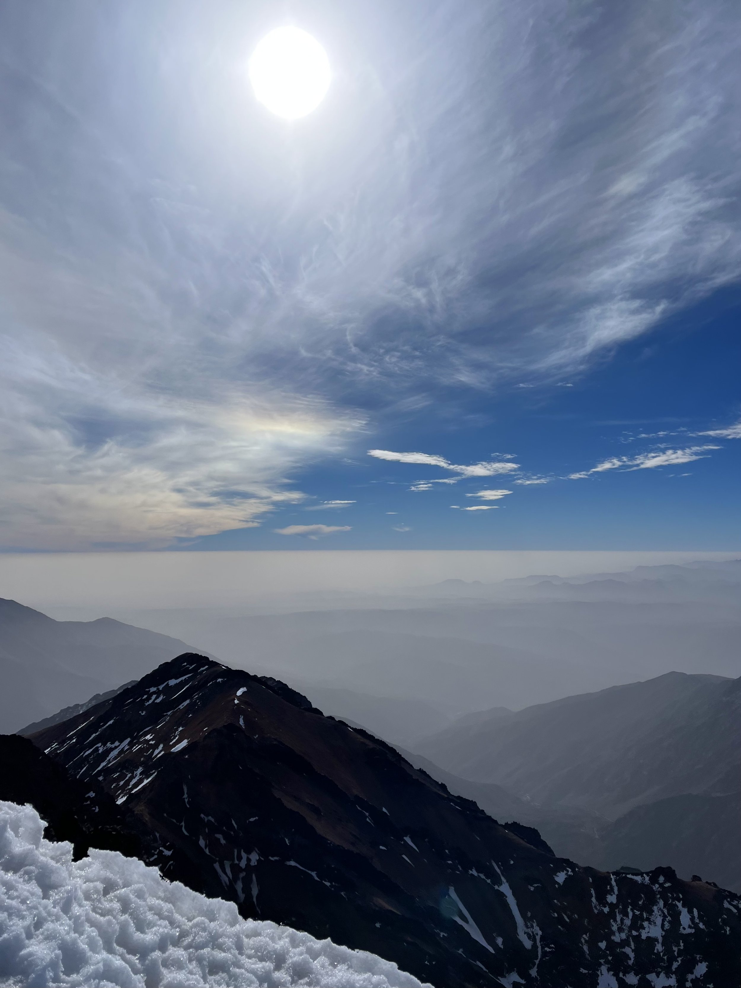 Snowy mountain peak under a bright sun with a cloudy sky.