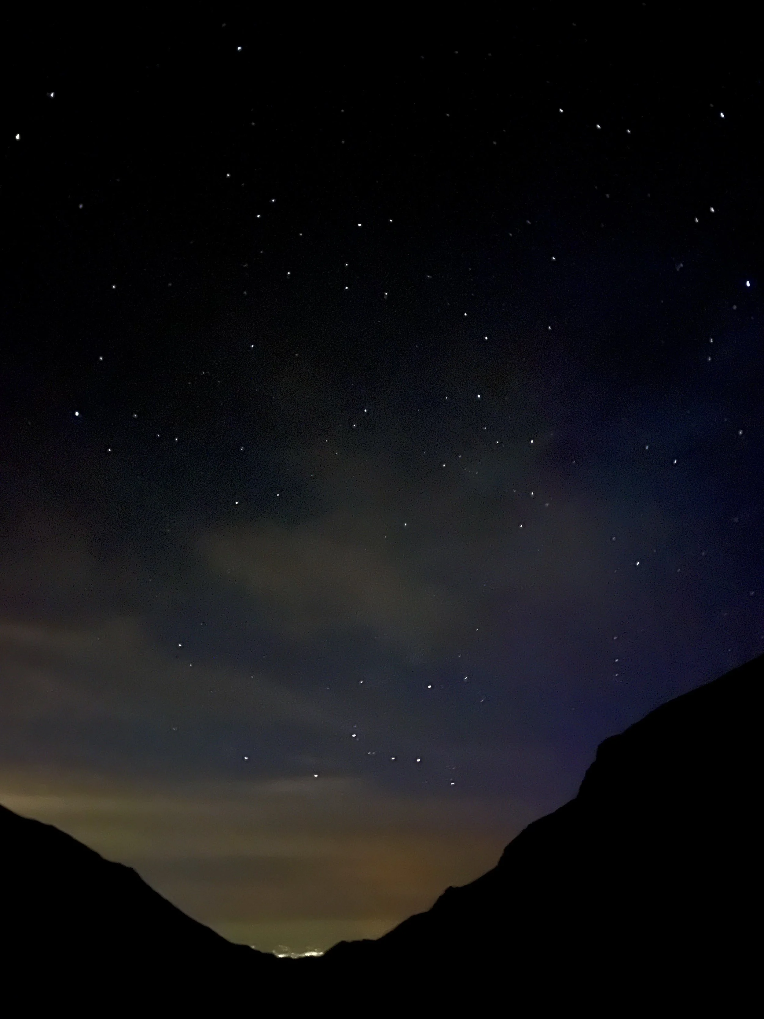 Starry night sky with silhouettes of mountains in the foreground.