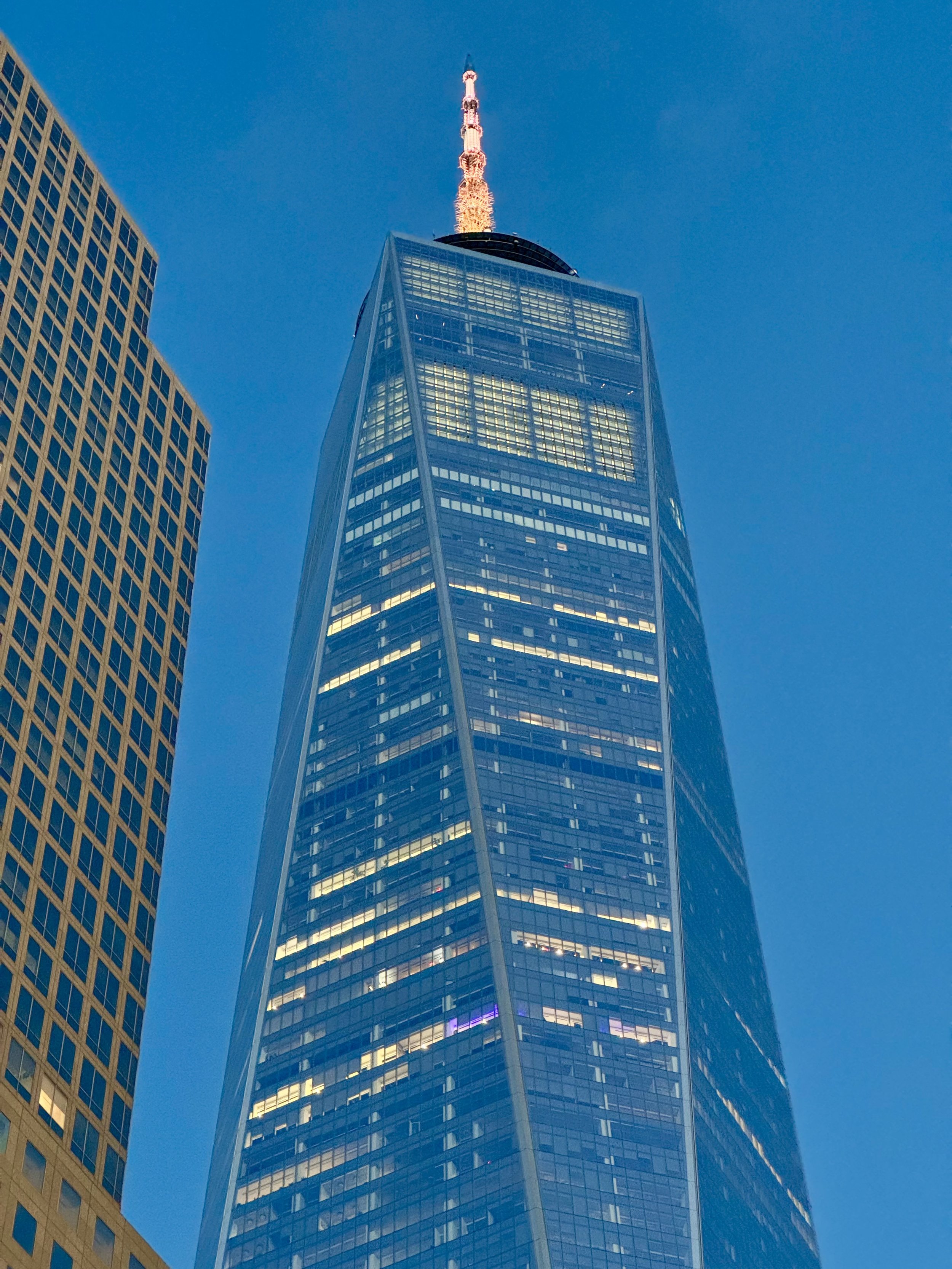 One World Trade Center skyscraper in New York City, viewed from below against a blue sky.