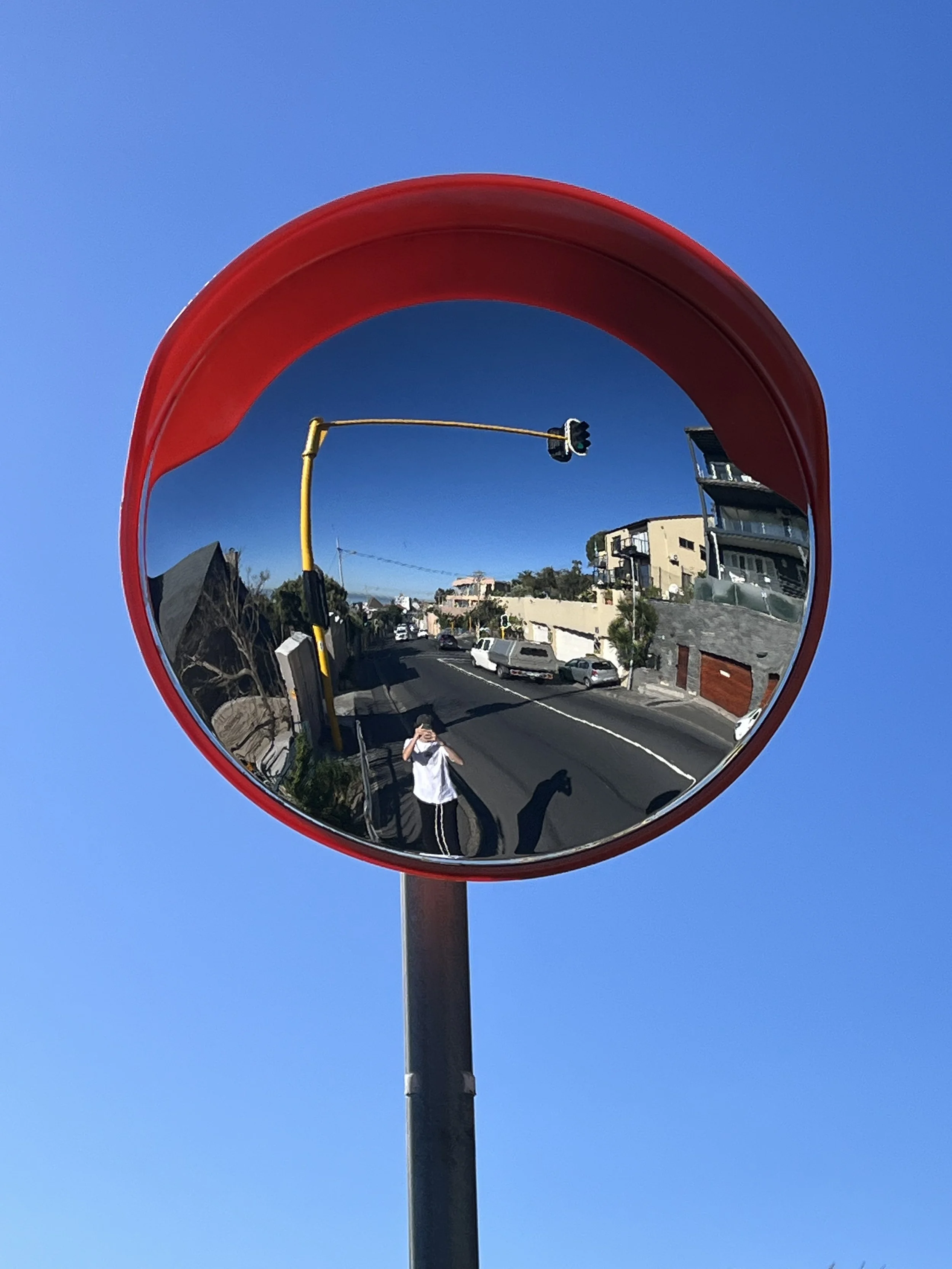 Round convex traffic mirror reflecting a street scene with a person and buildings under a clear blue sky.