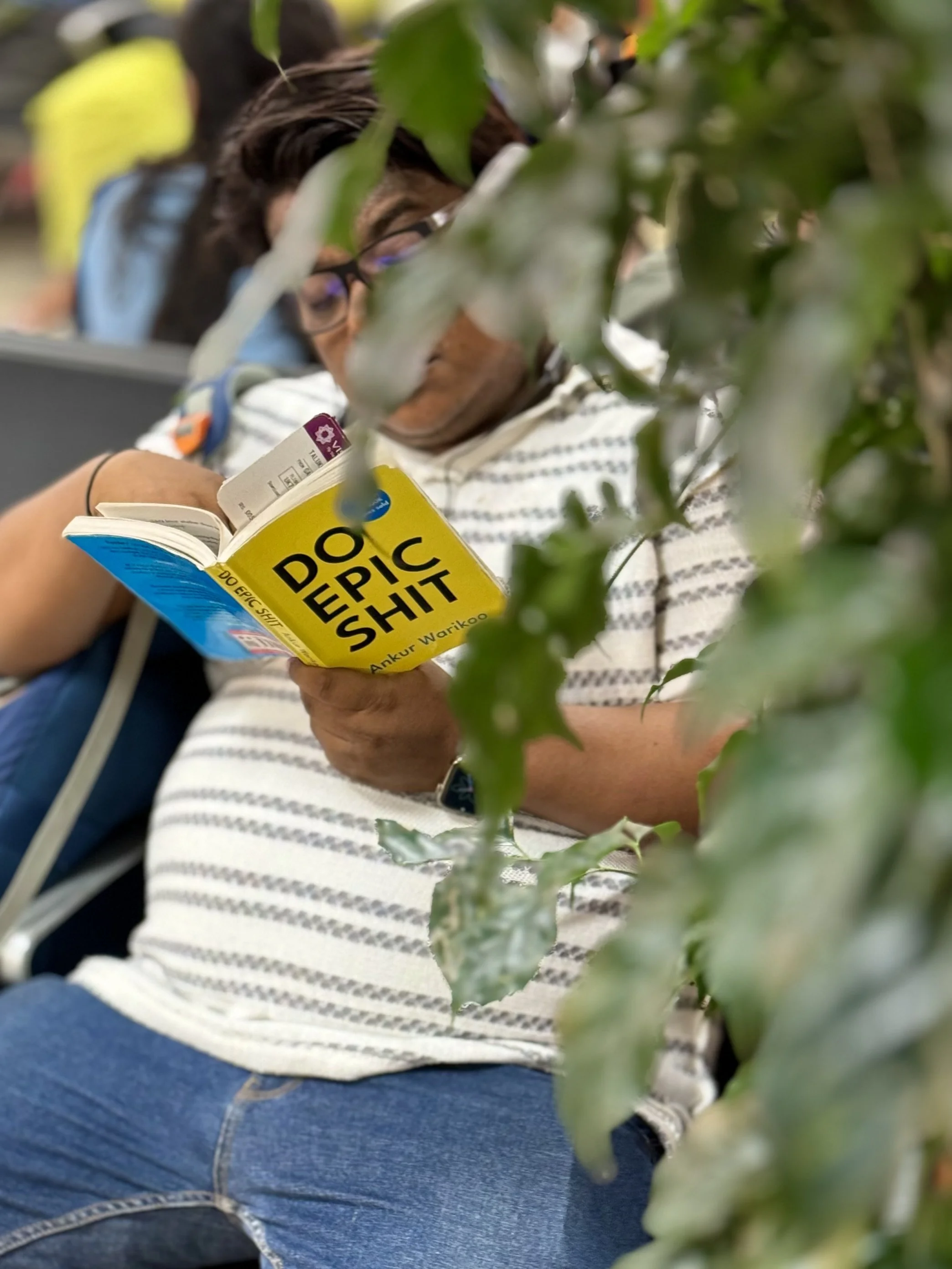 Person reading a book titled 'Do Epic Shit' while sitting, partially obscured by a plant.