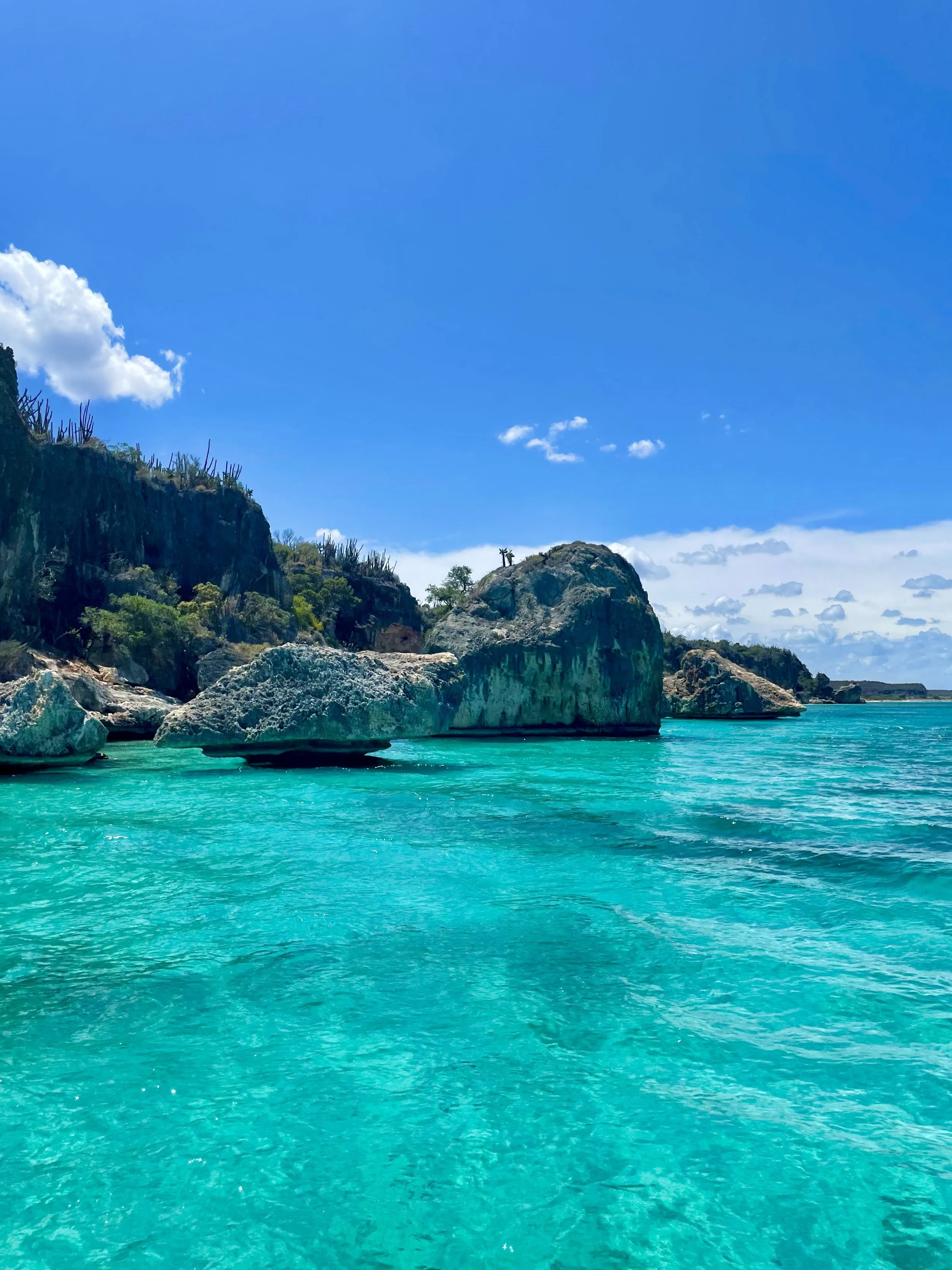 Tropical landscape with turquoise water, rocky cliffs, and blue sky.