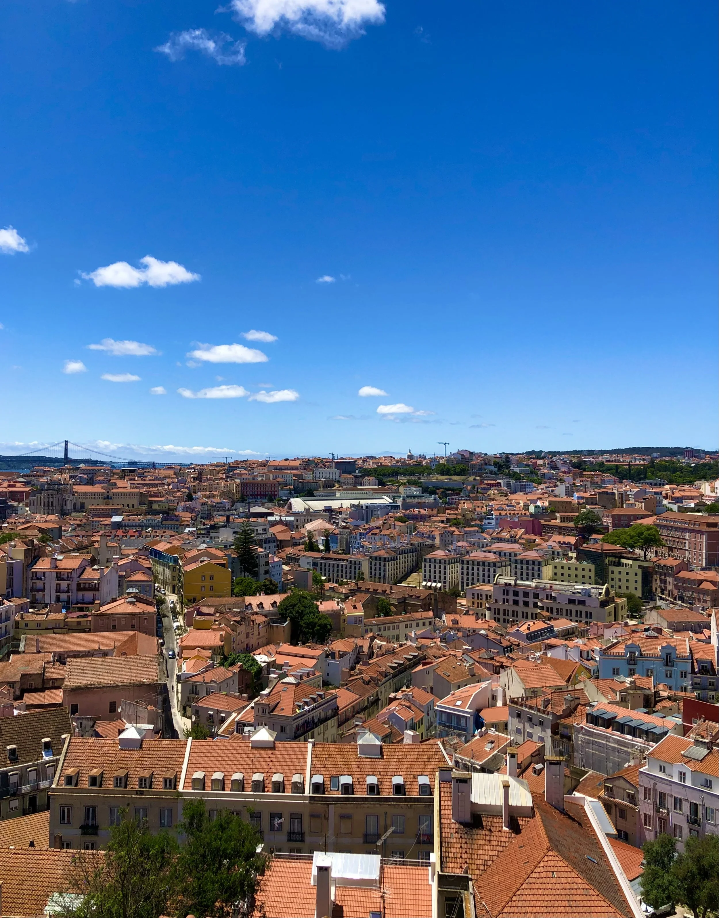 Panoramic view of a city with red-tiled roofs under a clear blue sky with scattered clouds.