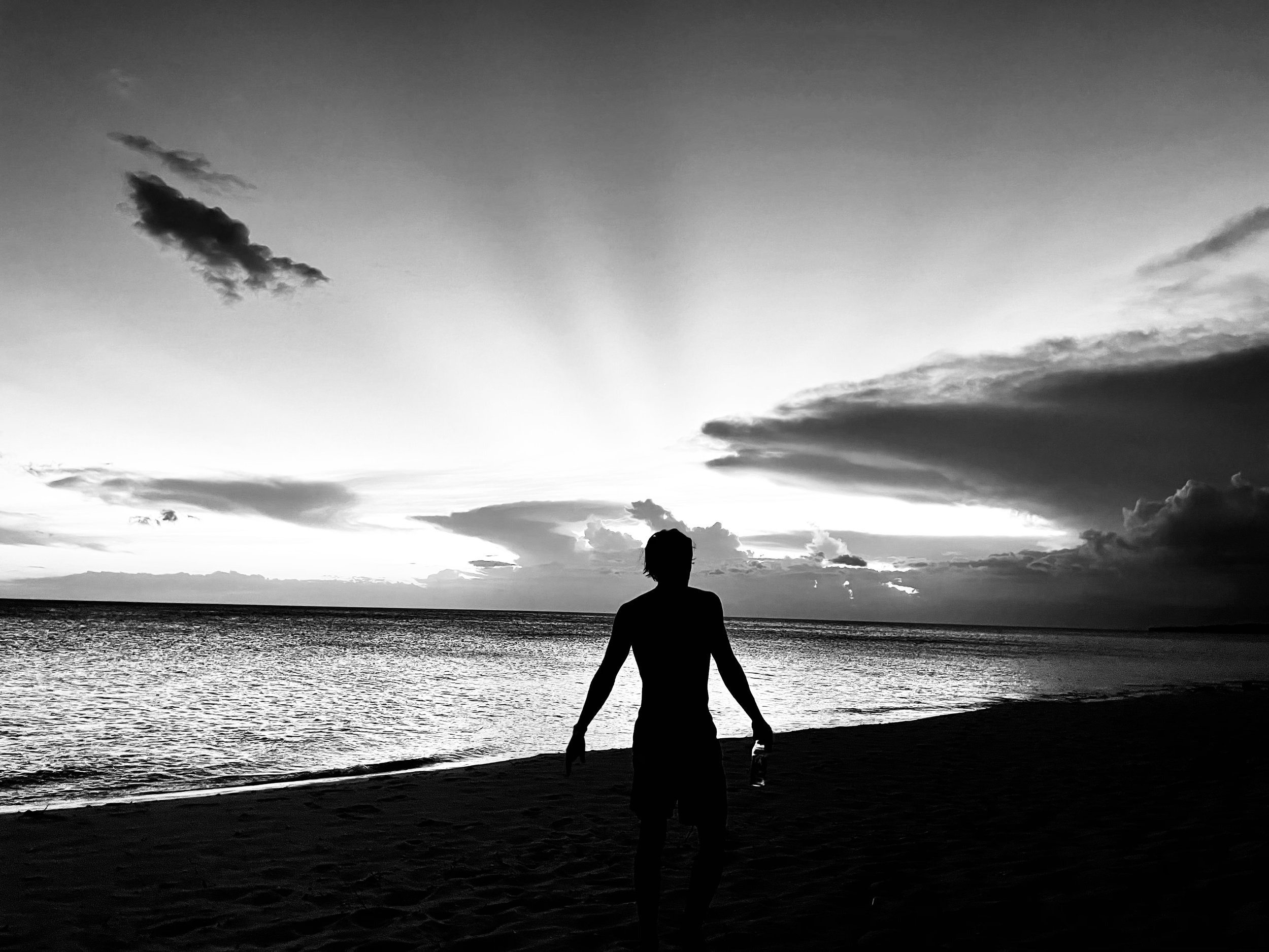 Silhouette of person on beach during sunset with dramatic clouds.