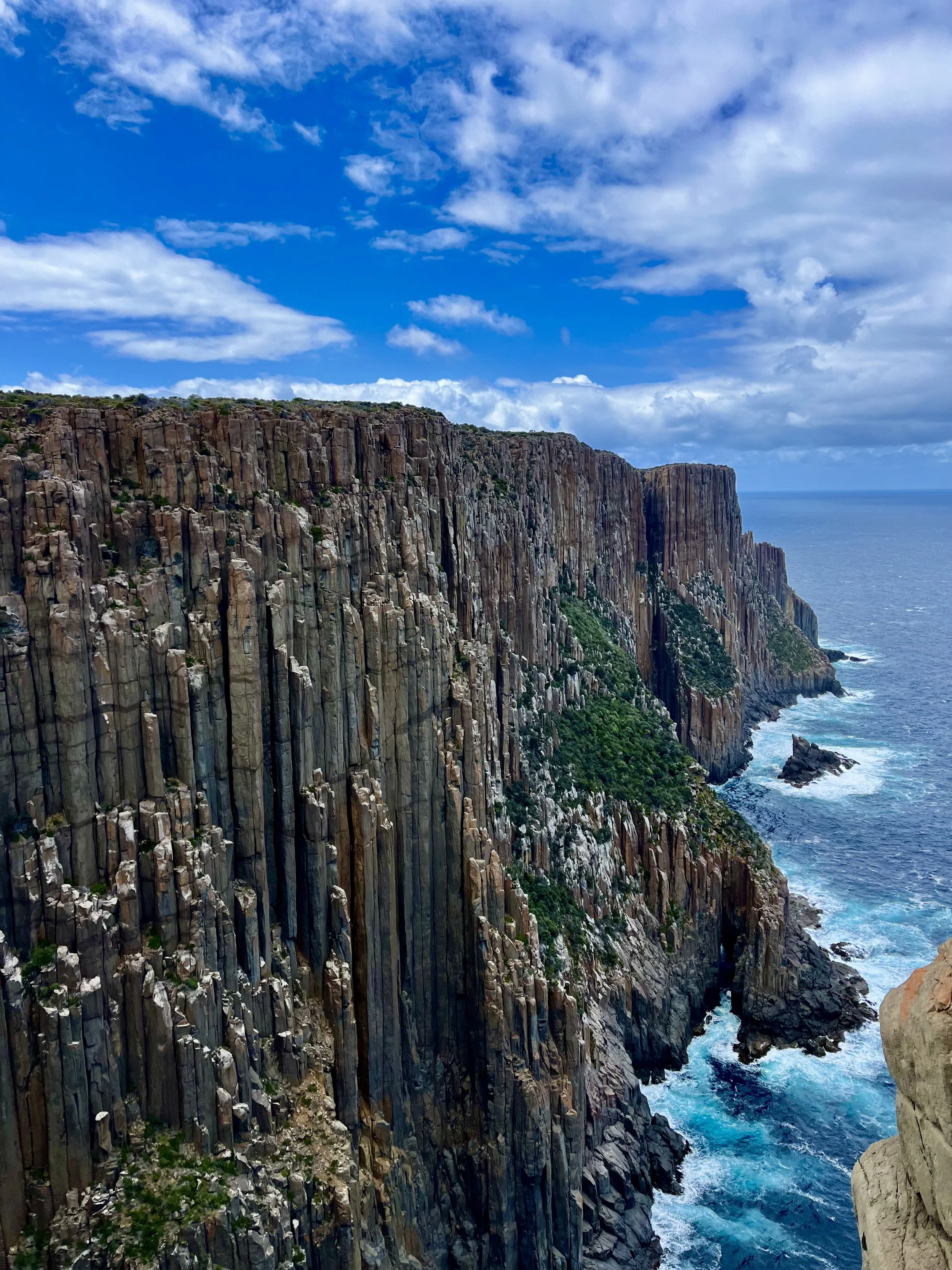 Dramatic coastal cliffs with vertical rock formations overlooking the ocean under a partly cloudy sky.