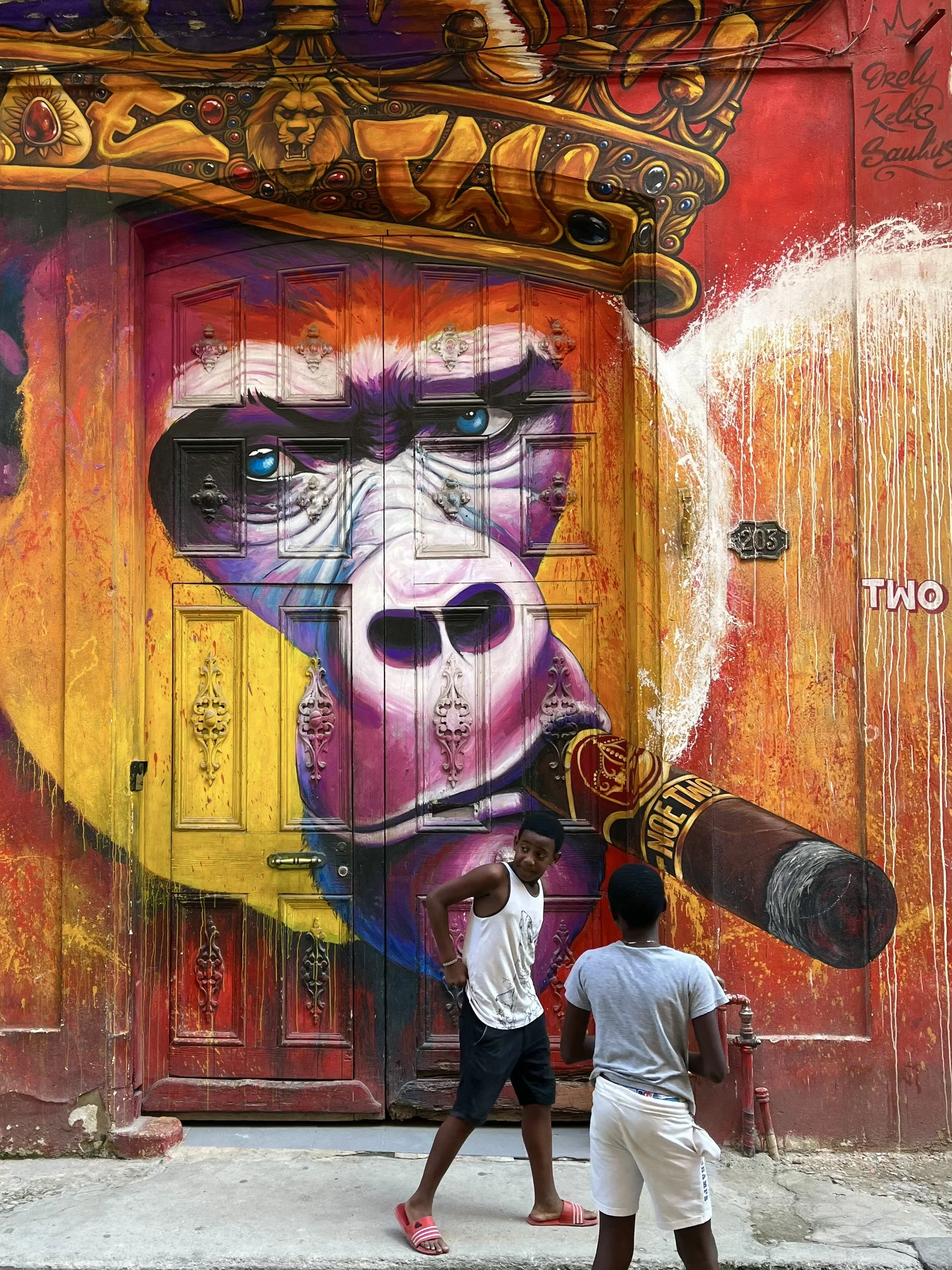 Colorful street art mural of a gorilla wearing a crown with two people walking by.