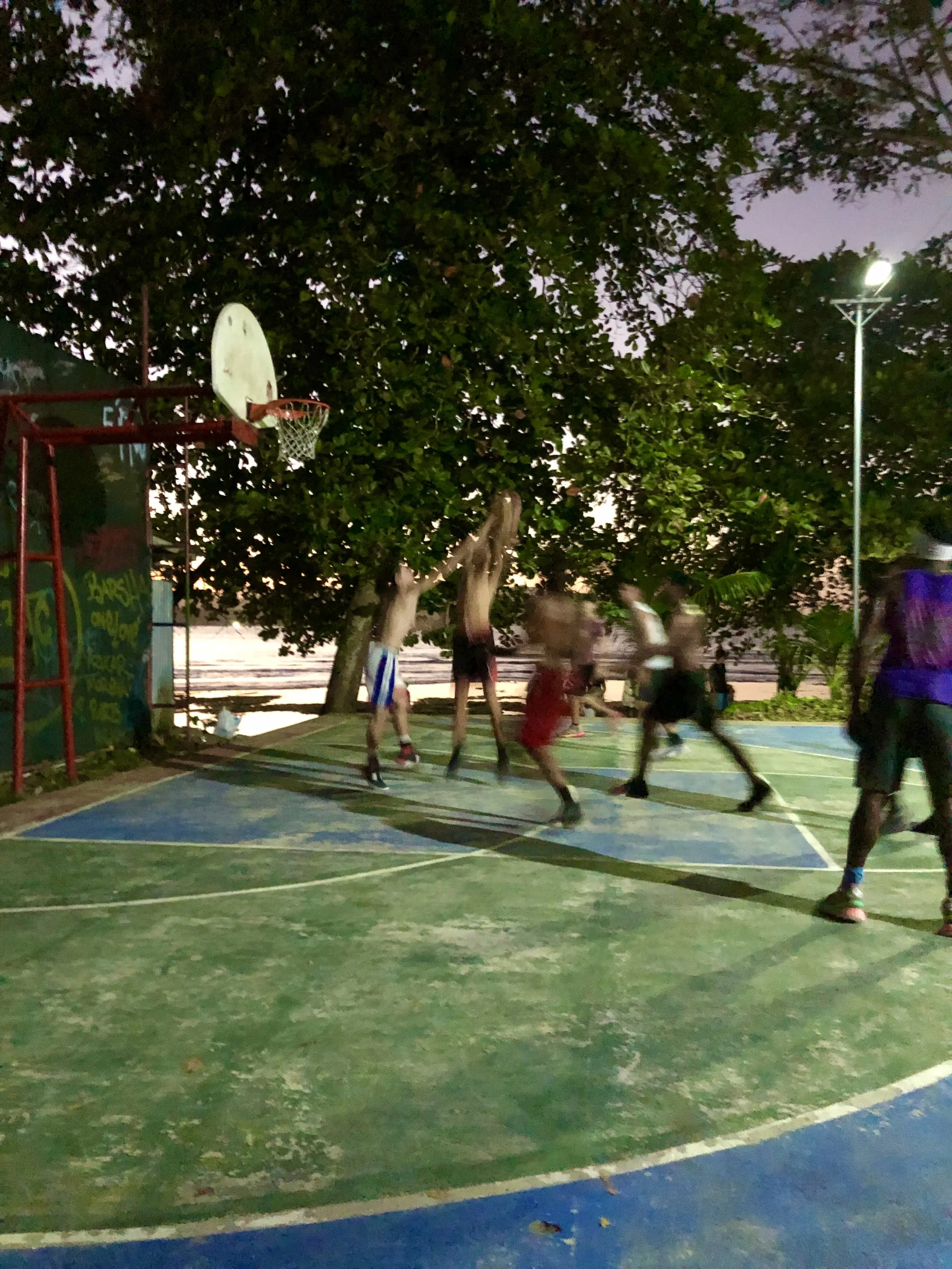 Group of people playing basketball on an outdoor court at dusk.