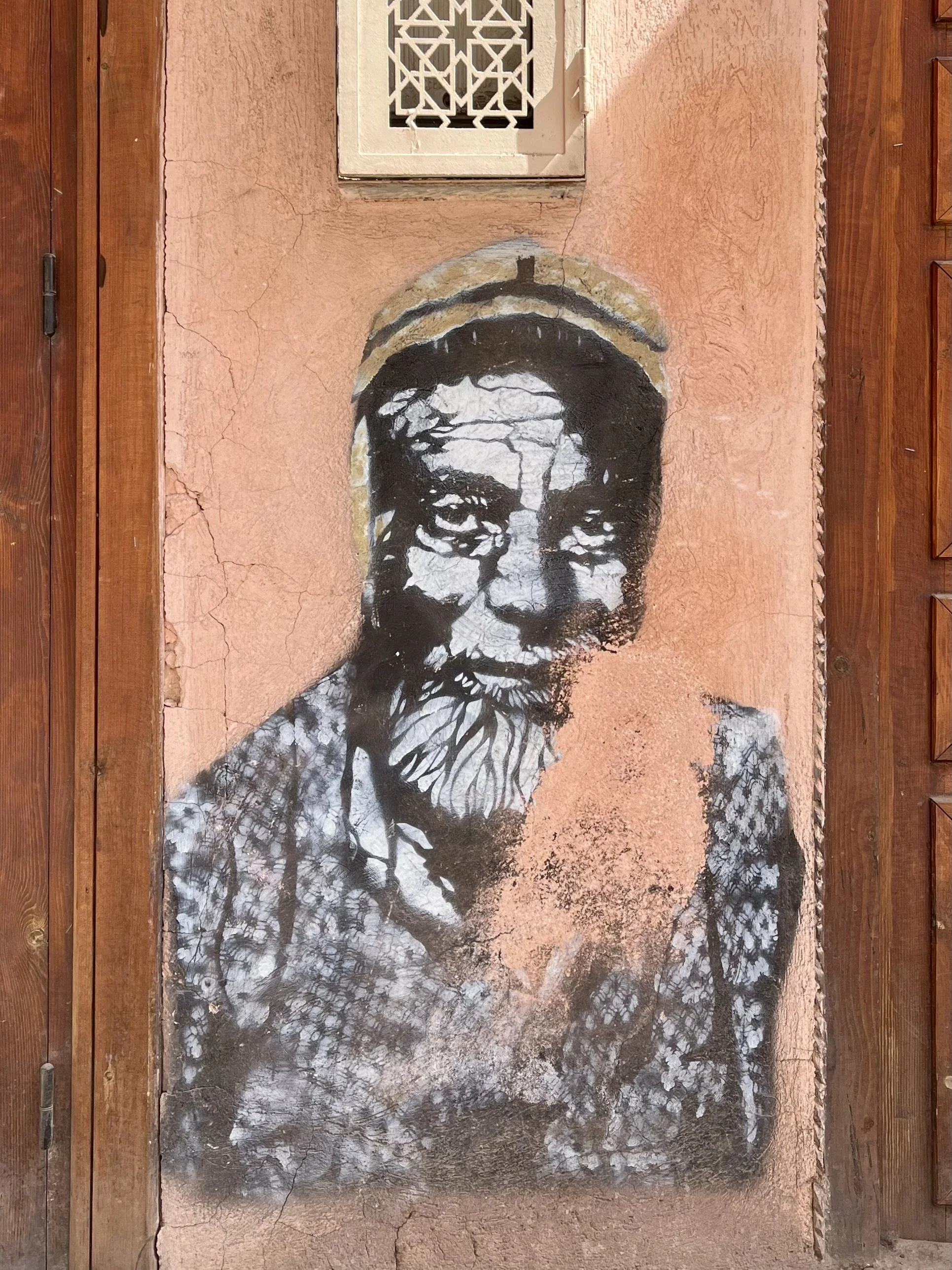Street art of a man's face on a textured wall next to a wooden door.