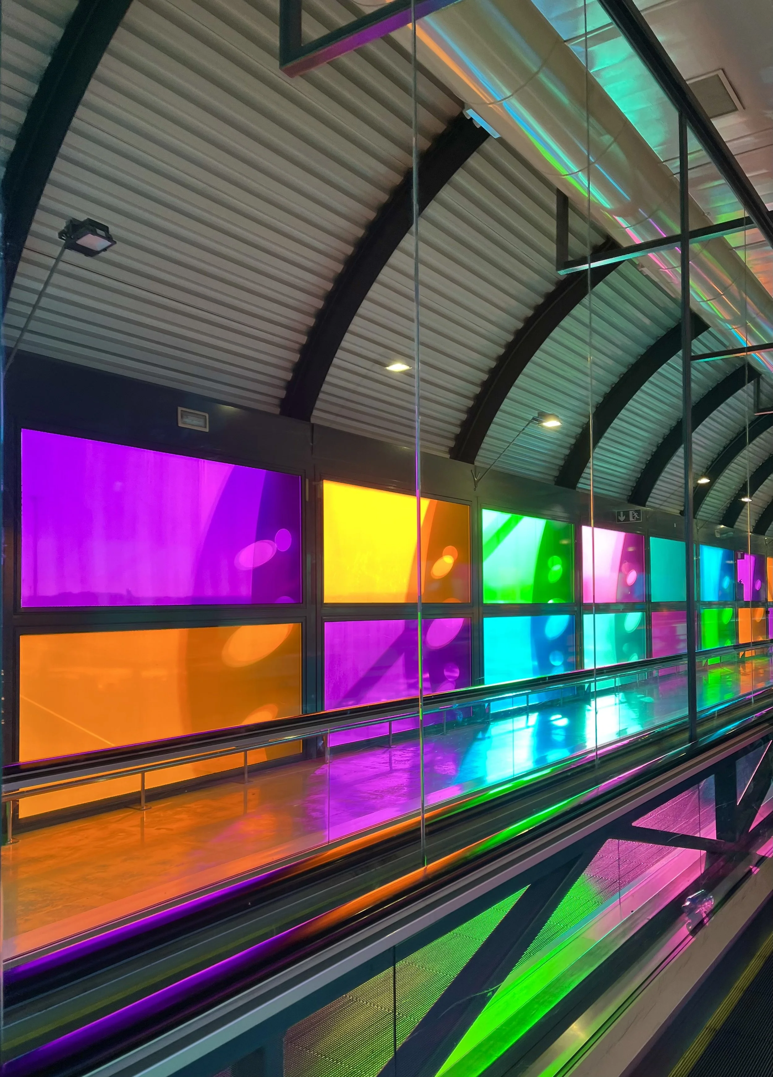 Colorful corridor with arched ceiling and rainbow-hued glass panels at an airport or modern building.