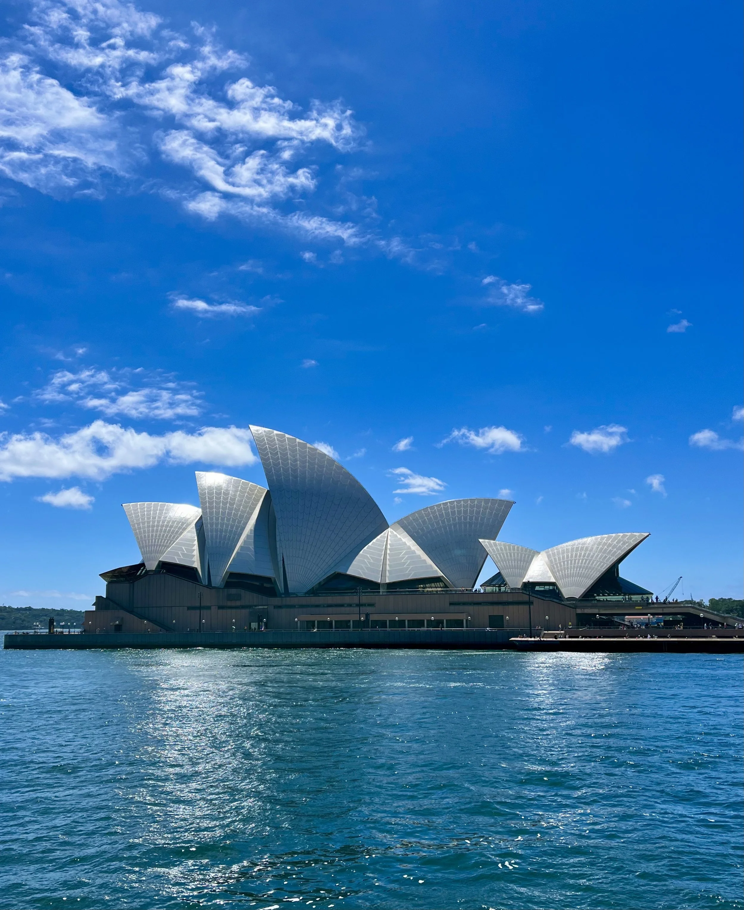 Sydney Opera House against a blue sky with water in the foreground.