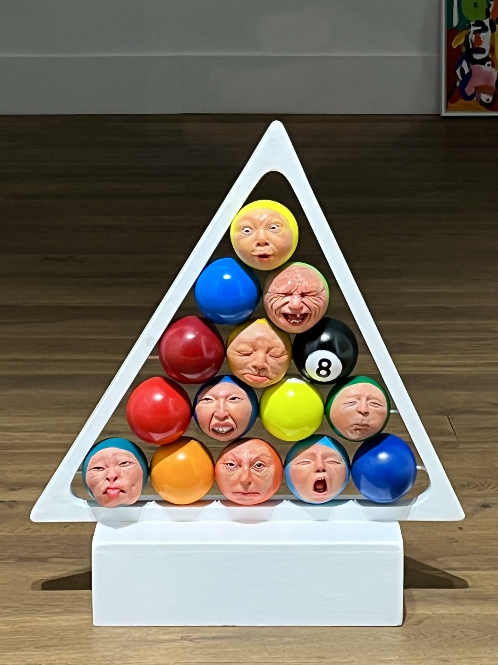 Artistic pool balls with human faces arranged in a triangular rack.