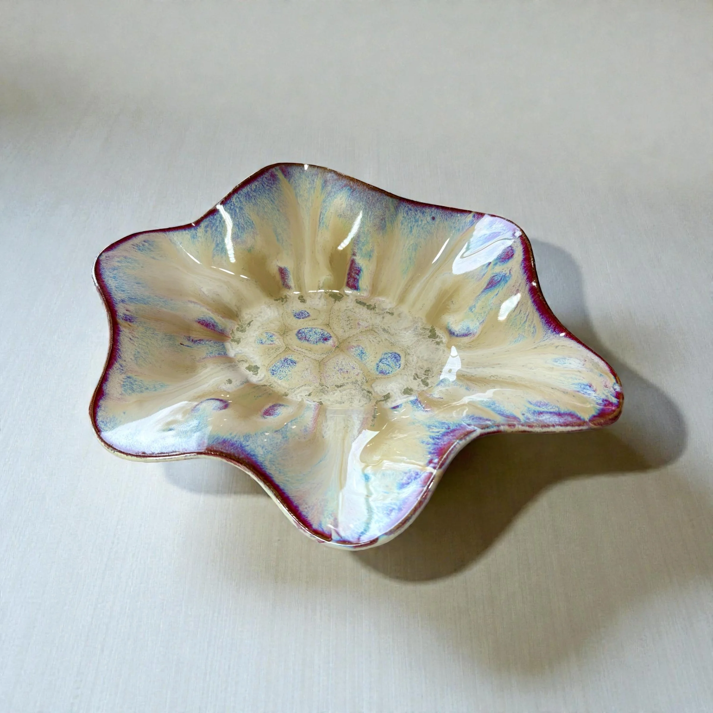 A decorative ceramic bowl with a flower-shaped rim, glazed with iridescent colors and seated on a light-colored surface.