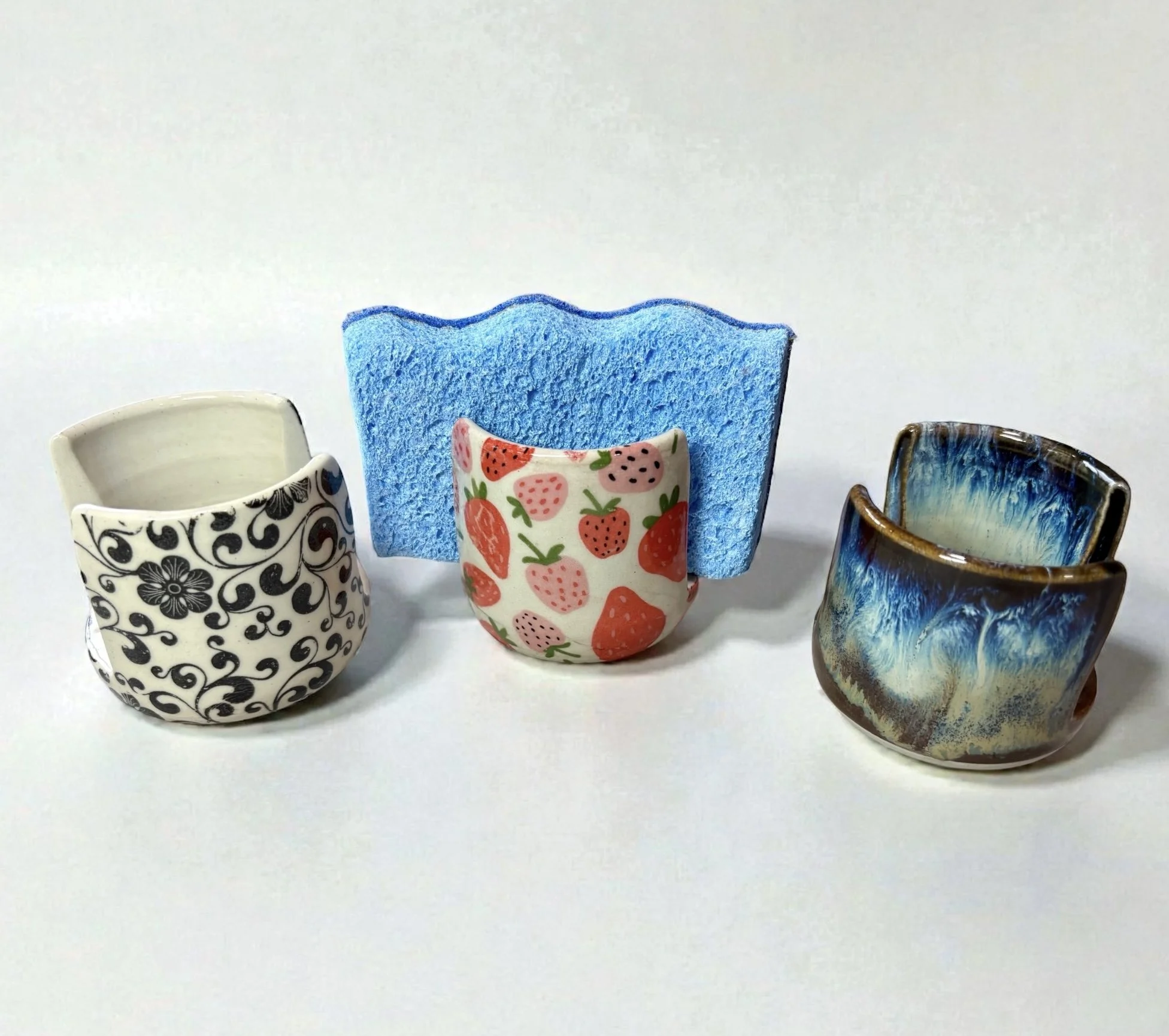 Three decorated ceramic cups and a blue sponge.