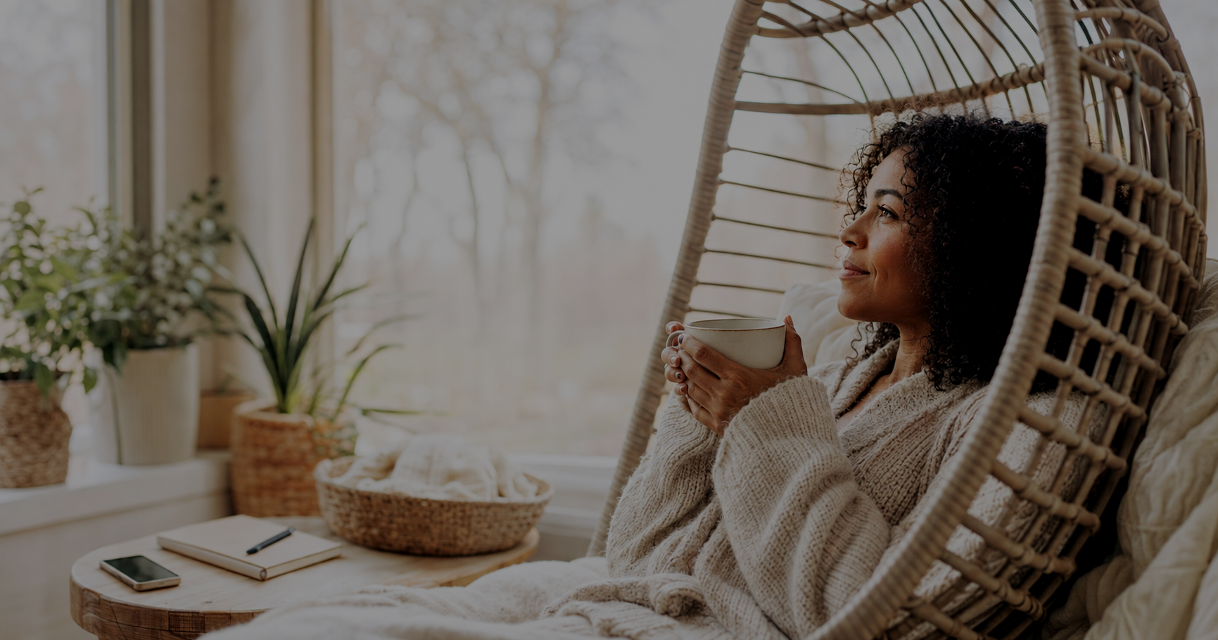 A warm, peaceful woman relaxes in a cozy hanging chair with a mug beside her and her phone placed face down, reflecting the calm that comes from unplugging, releasing clutter, and making space for a lighter, more intentional 2027.