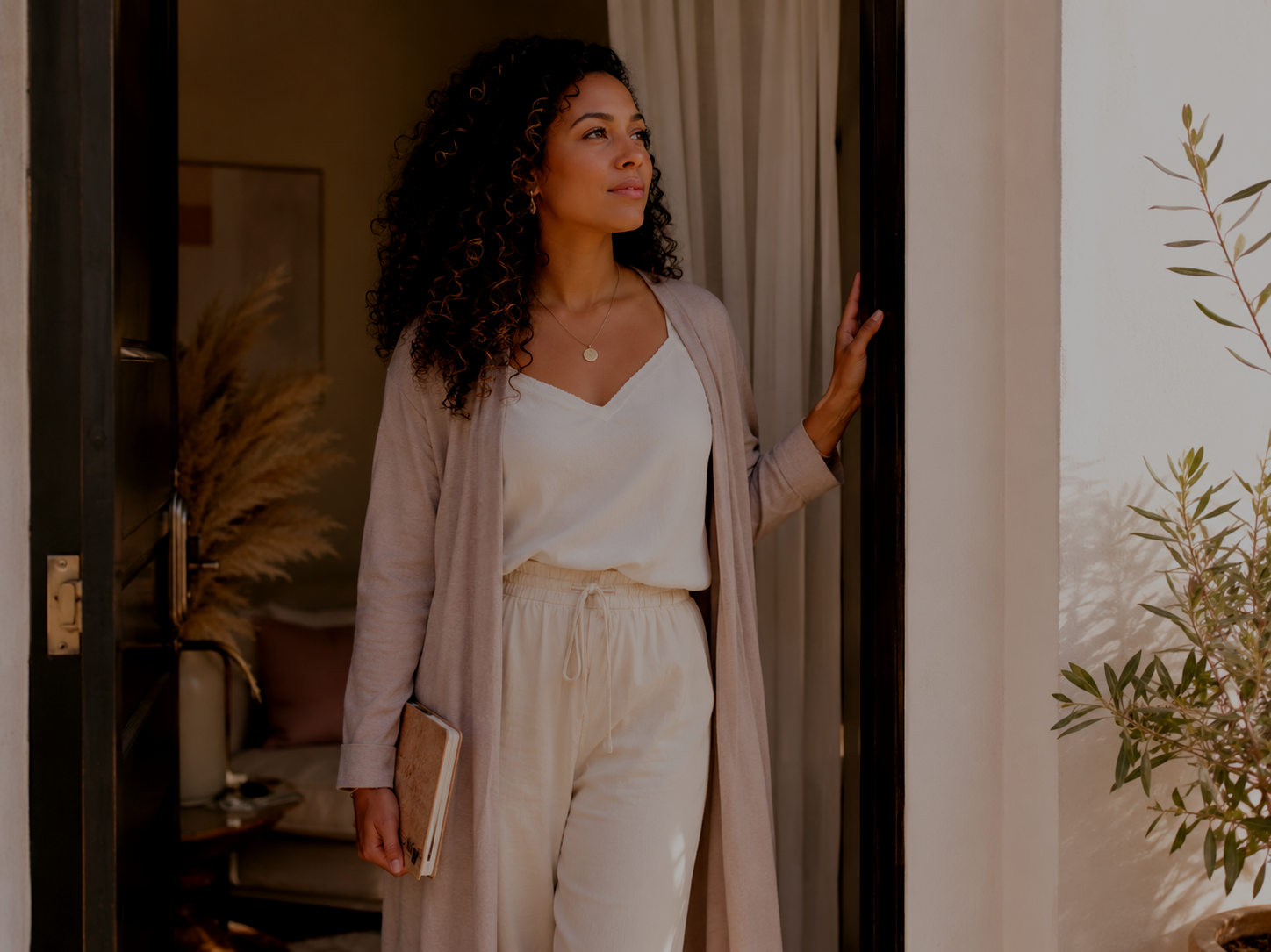 Afro-Latina woman standing in a sunlit doorway holding a journal, symbolizing quiet courage, vulnerability, and choosing to show up even when afraid.