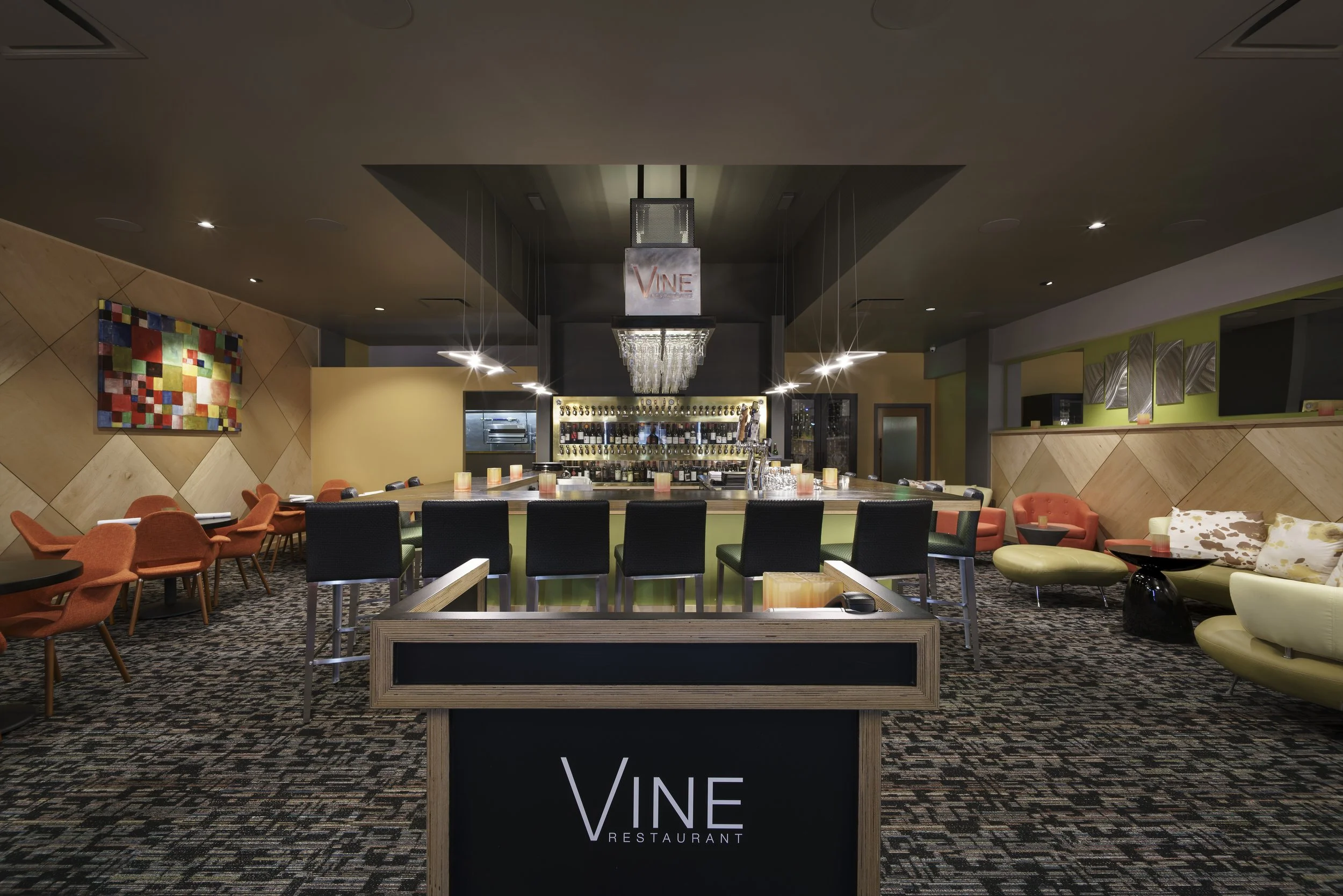 Interior of a modern restaurant with a bar, colorful seating, abstract wall art, and a purple and black color scheme.