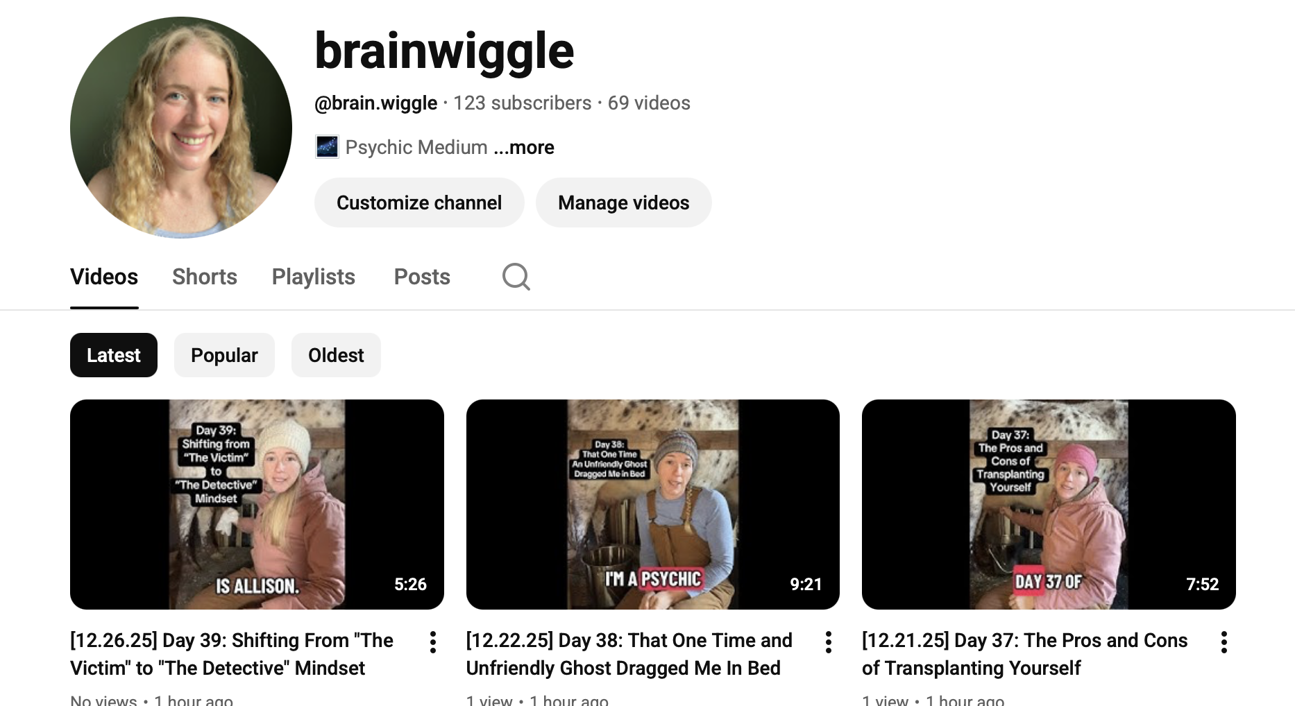 Screenshot of a YouTube channel profile named 'brainwiggle' featuring a profile photo of a smiling woman with blonde curly hair, and thumbnail previews of three videos from the channel's latest uploads showing women in cozy clothing with text overlays about psychic reading experiences.