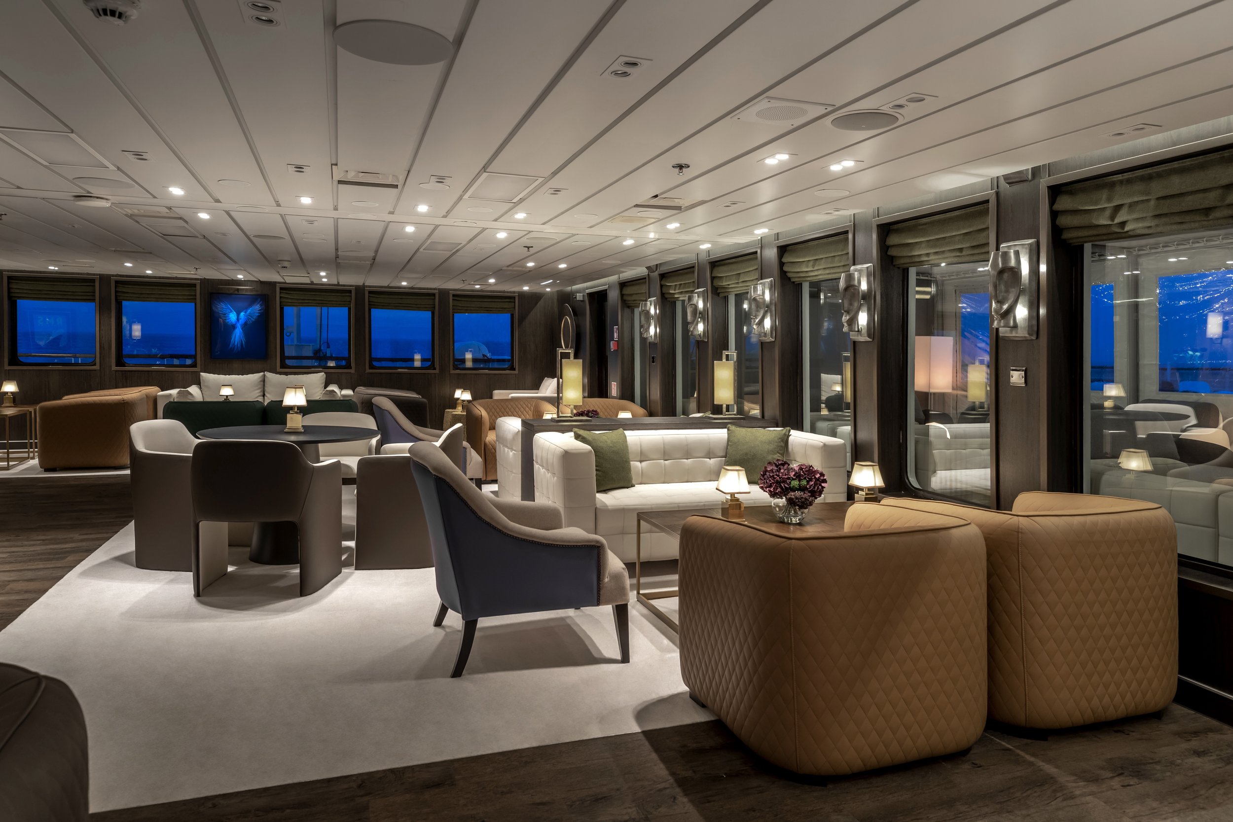 Luxurious lounge area with modern furniture, lamps, and large windows at night.