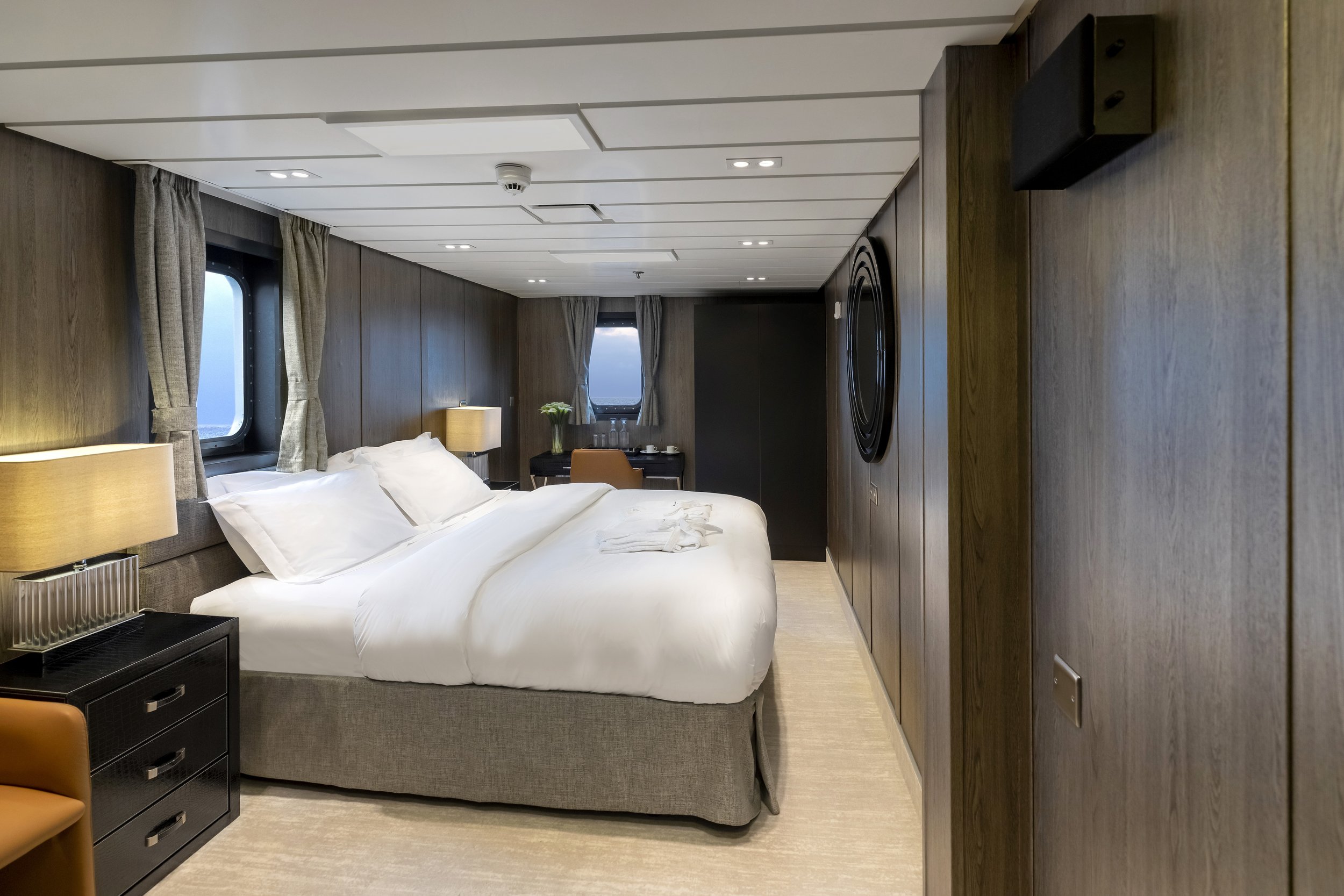 A hotel room with a large bed, nightstands with lamps, and windows with curtains.