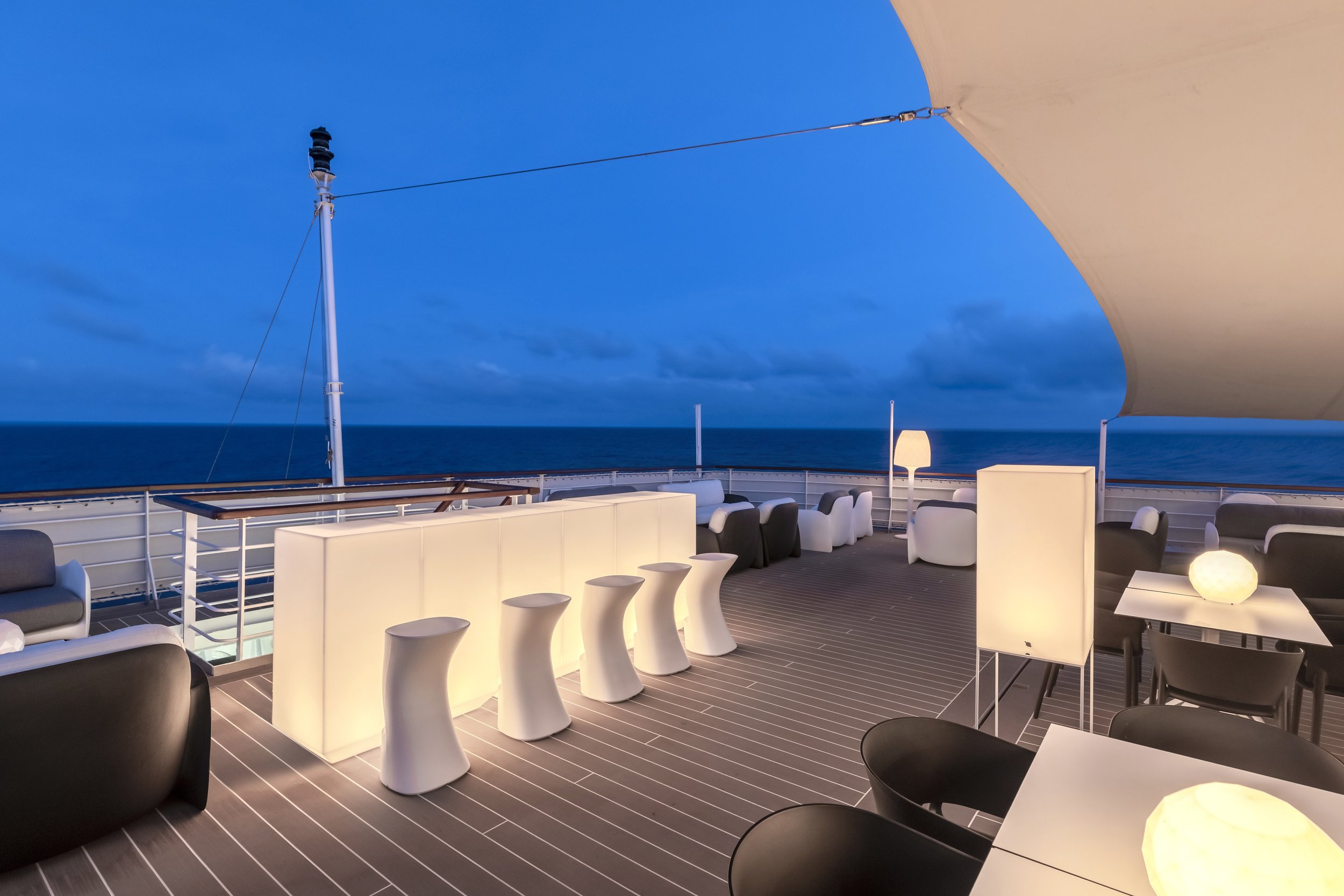 Outdoor lounge area on a ship deck at dusk with modern seating and ambient lighting, overlooking the ocean.