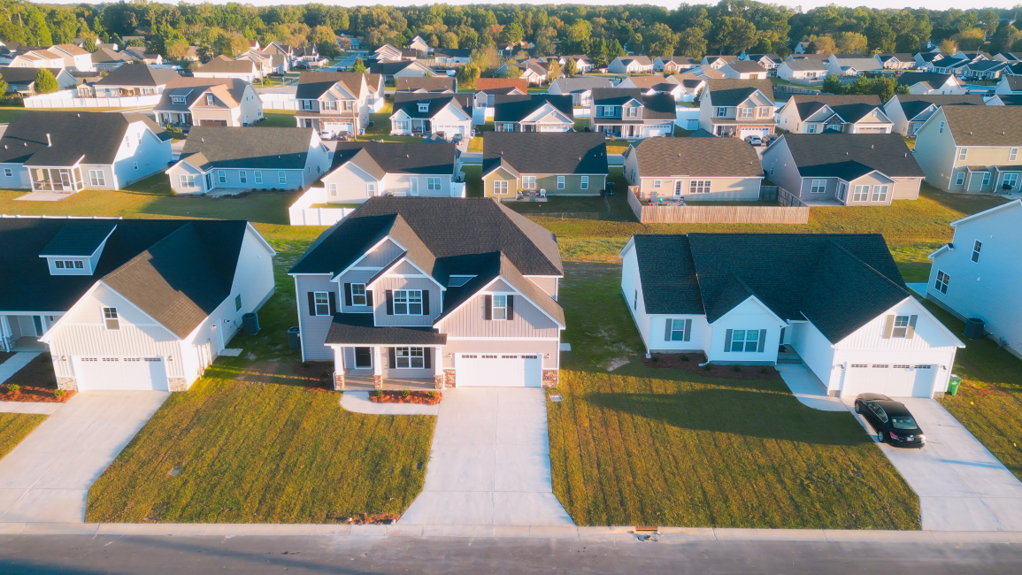 Aerial view of suburban houses with manicured lawns, driveways, and a neighborhood with many similar homes.