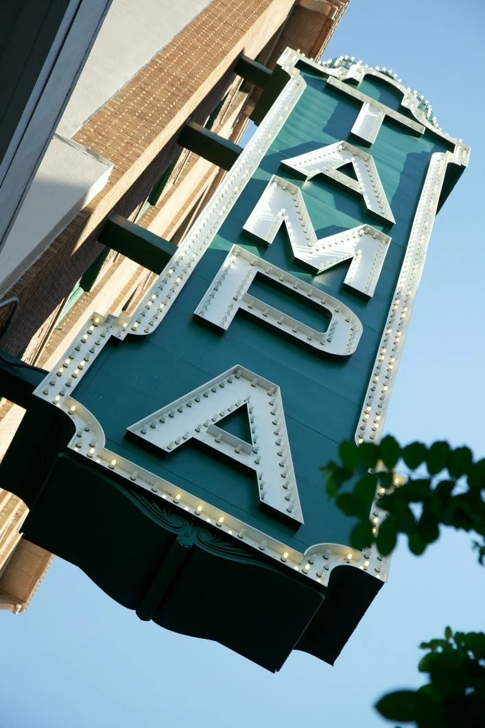 Vintage marquee sign with the word "RAFFLE" in large white letters and light bulbs, hanging vertically against a building with a blue sky background.