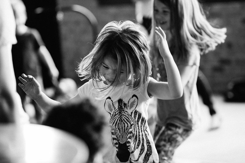 Black and white photo of children dancing, with a girl in a zebra print shirt in the foreground.