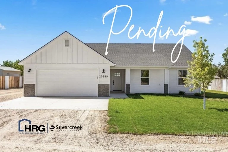 A newly built single-story house with a white exterior, gray roof, front garage, and small front yard with green grass and a tree on the right.