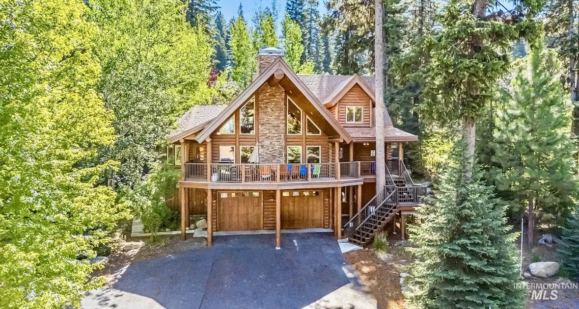 A large wooden house with multiple levels and a garage, surrounded by dense green trees, in a forested area.
