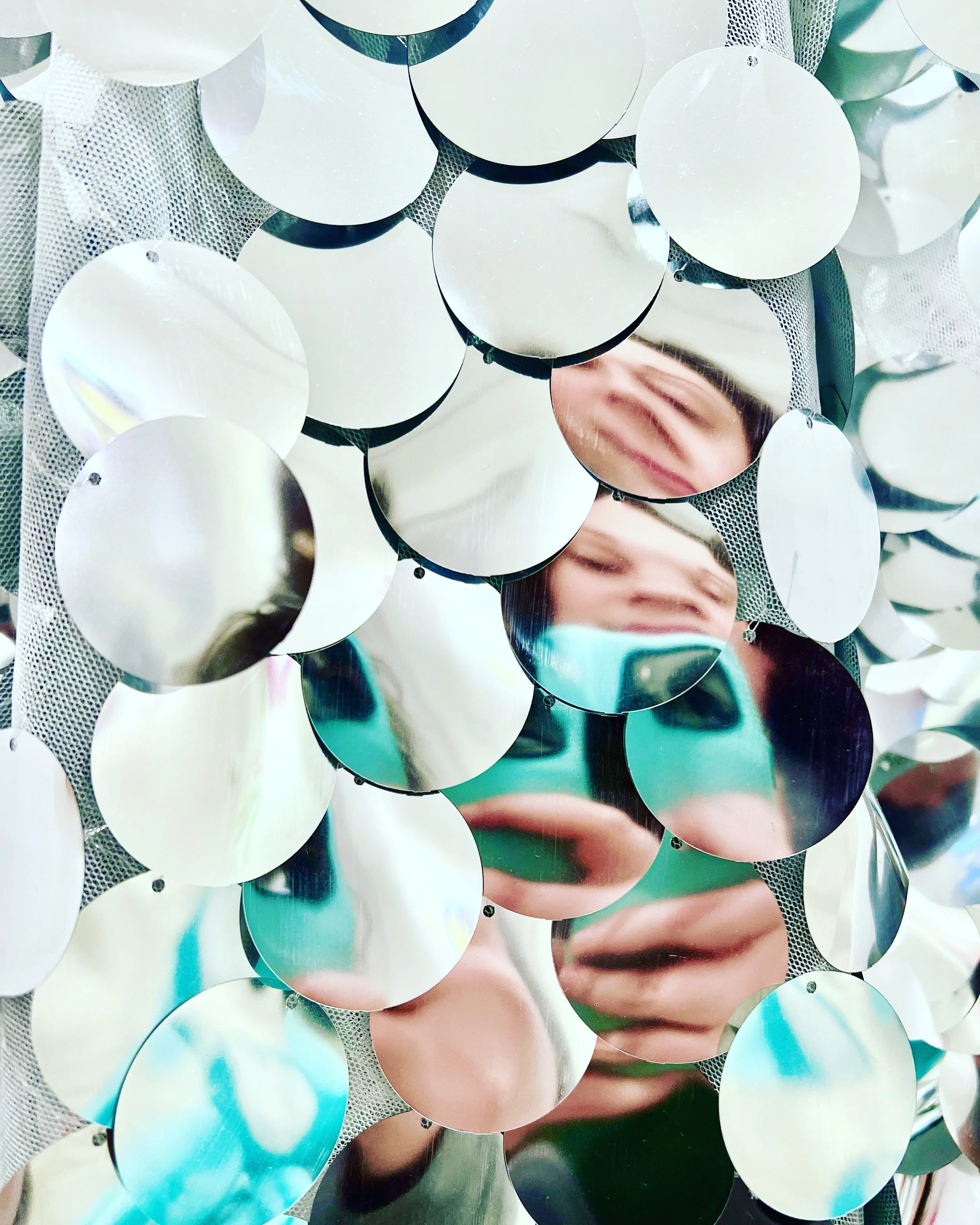 Close-up of a decorative photo frame made of circular mirrors, reflecting a person taking a photograph.