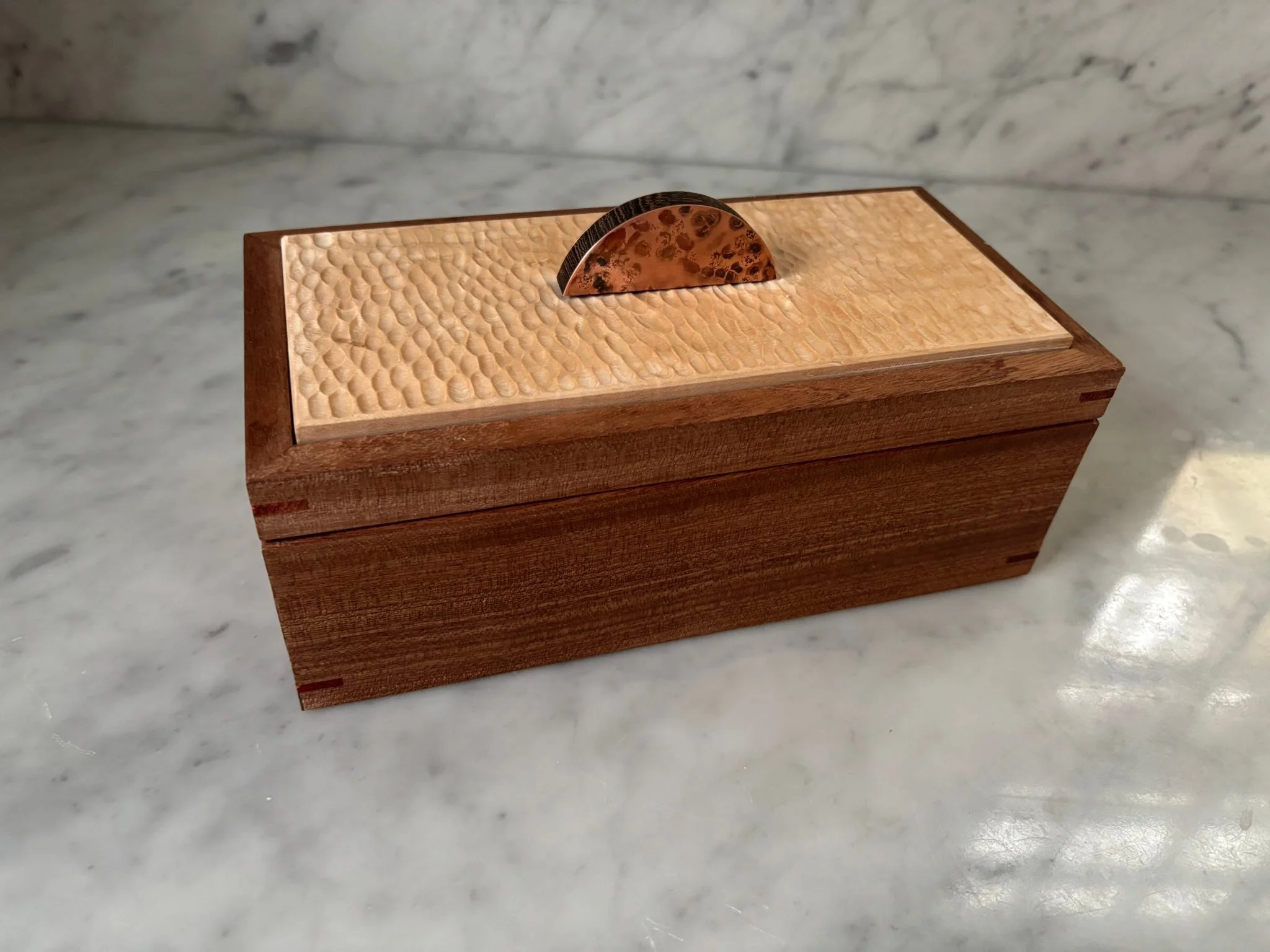 Working on a box which is one of four commissioned pieces. These involve a large amount of hand tool work. Top is maple with a handcarved/textured surface. Copper/wenge decorative handle. Box is constructed of sapele with padauk splines. Inside is bi