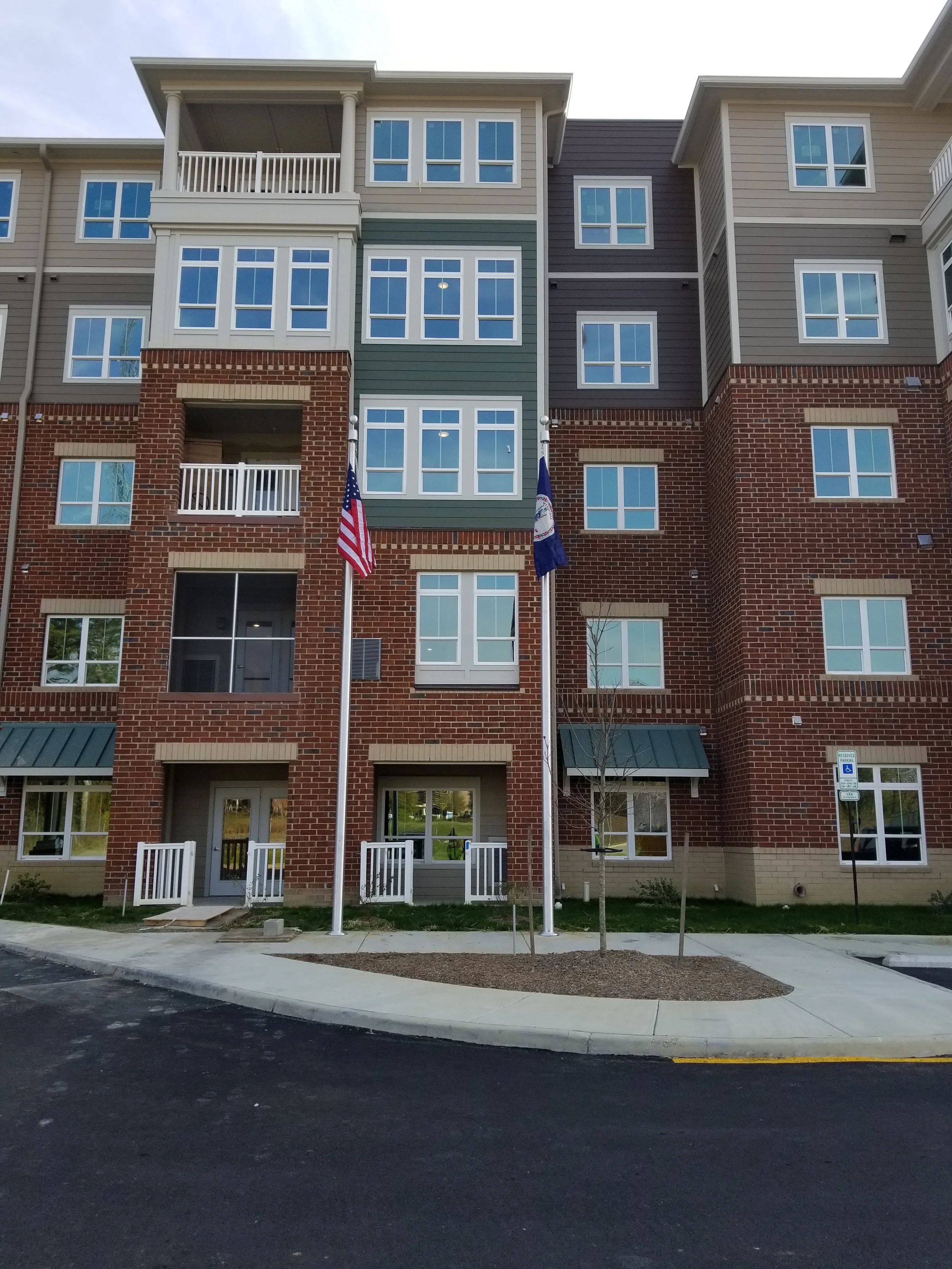 Four-story brick and siding apartment building with balconies and multiple windows, displaying two flags on poles.