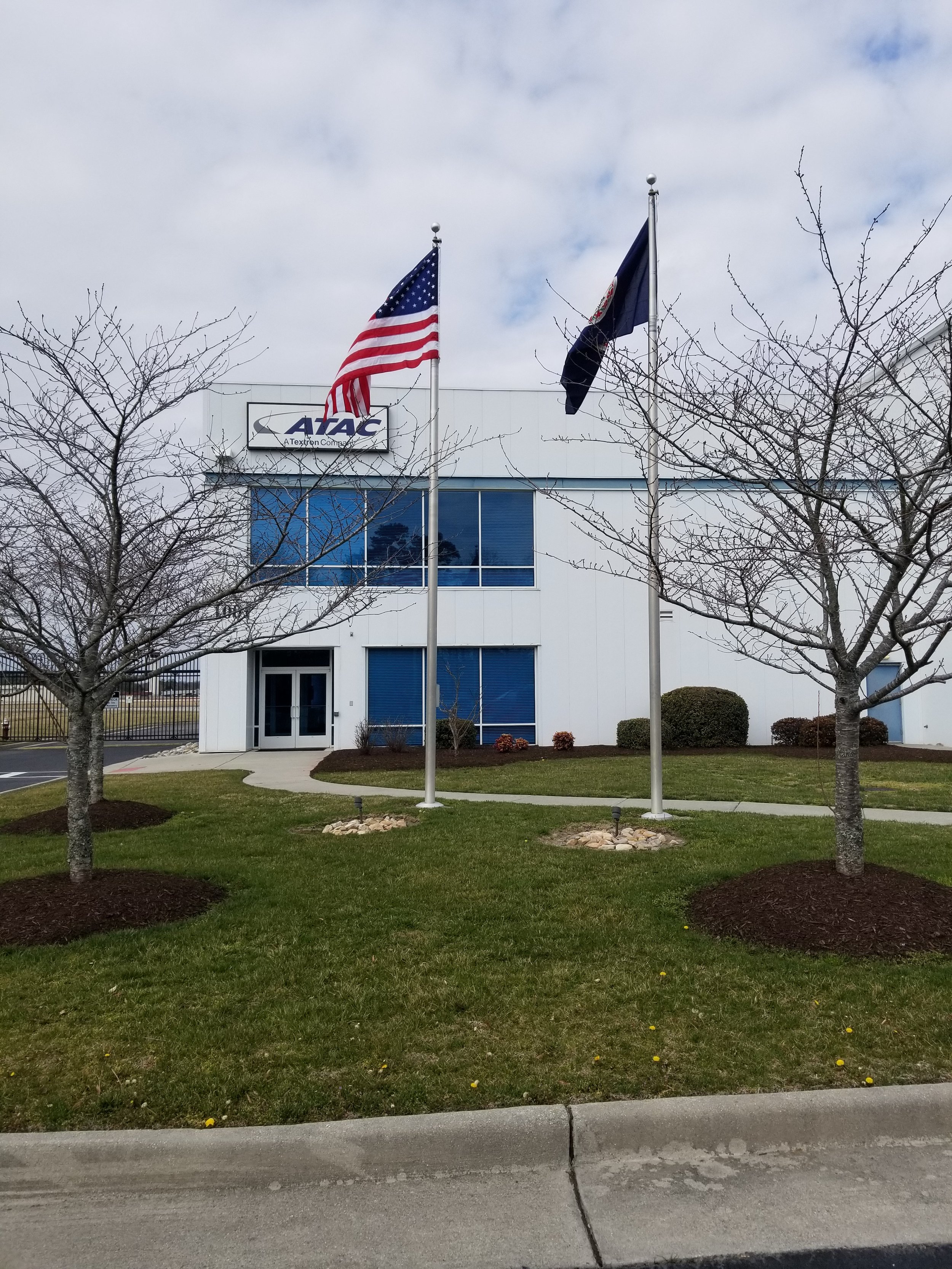Building exterior with American and another flag, labeled ATAC, surrounded by trees and grass