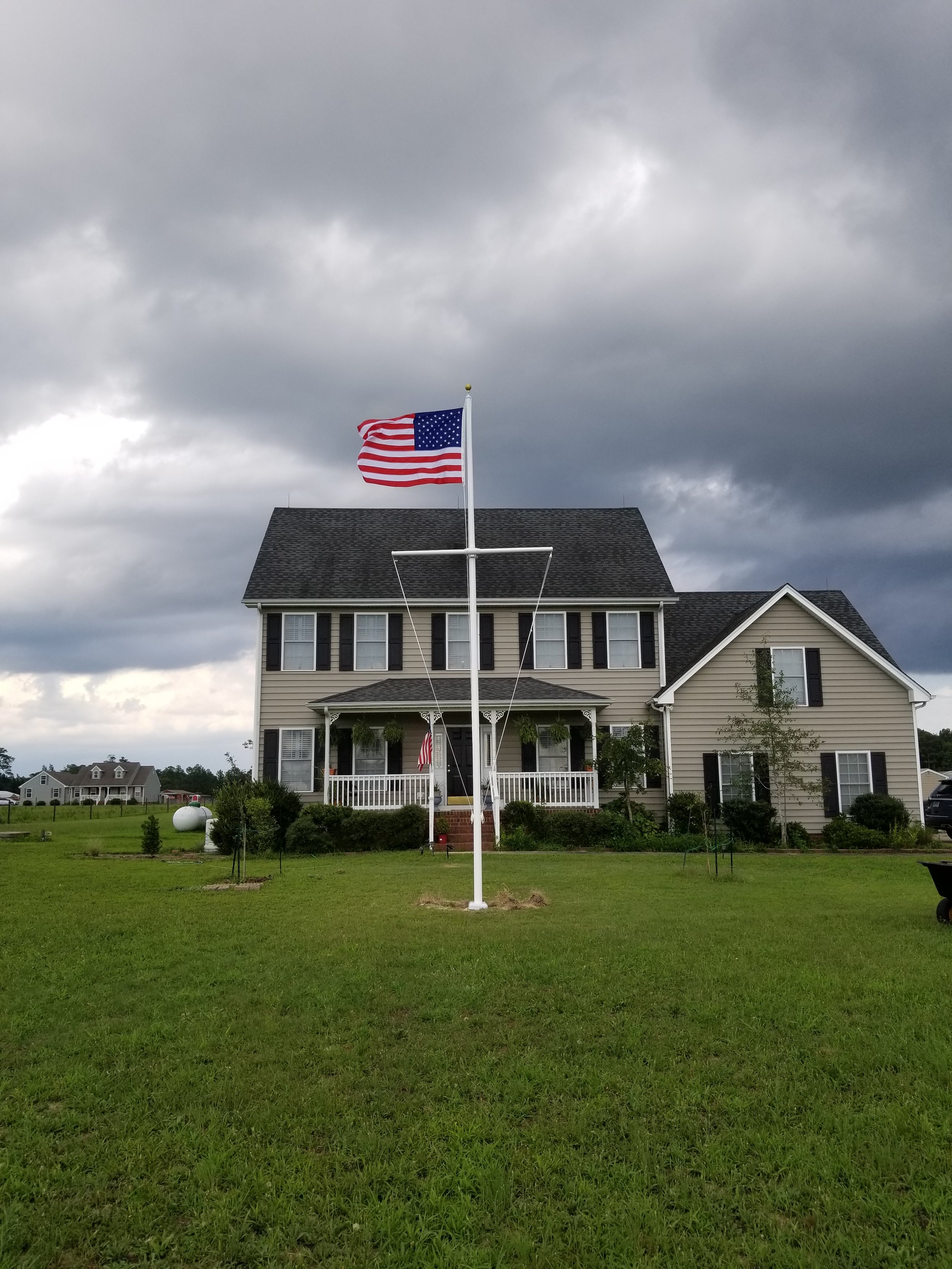 American flag flying in front of a two-story house with a large yard, under a cloudy sky.