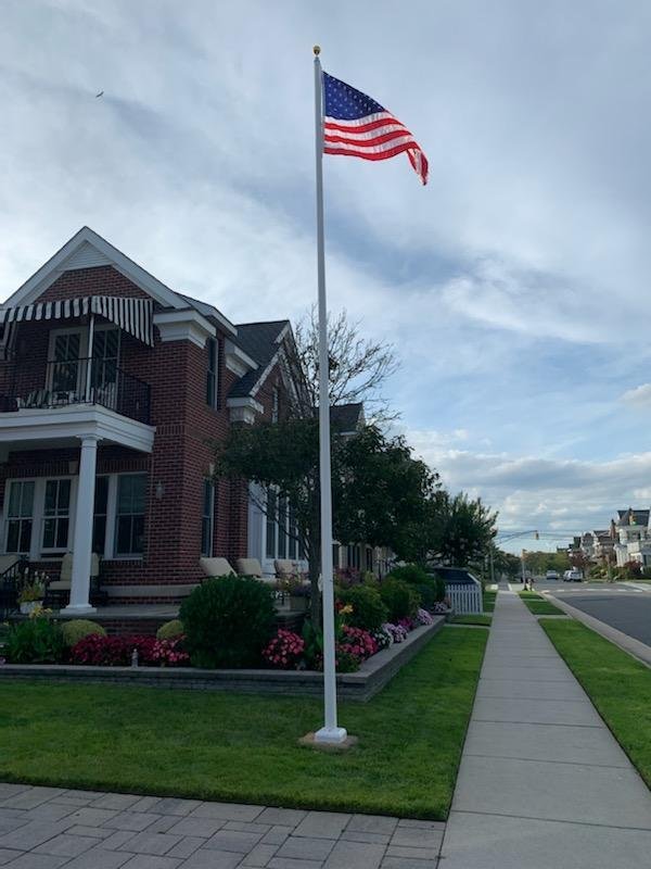 American flag on a flagpole in front of a brick house with a garden and sidewalk