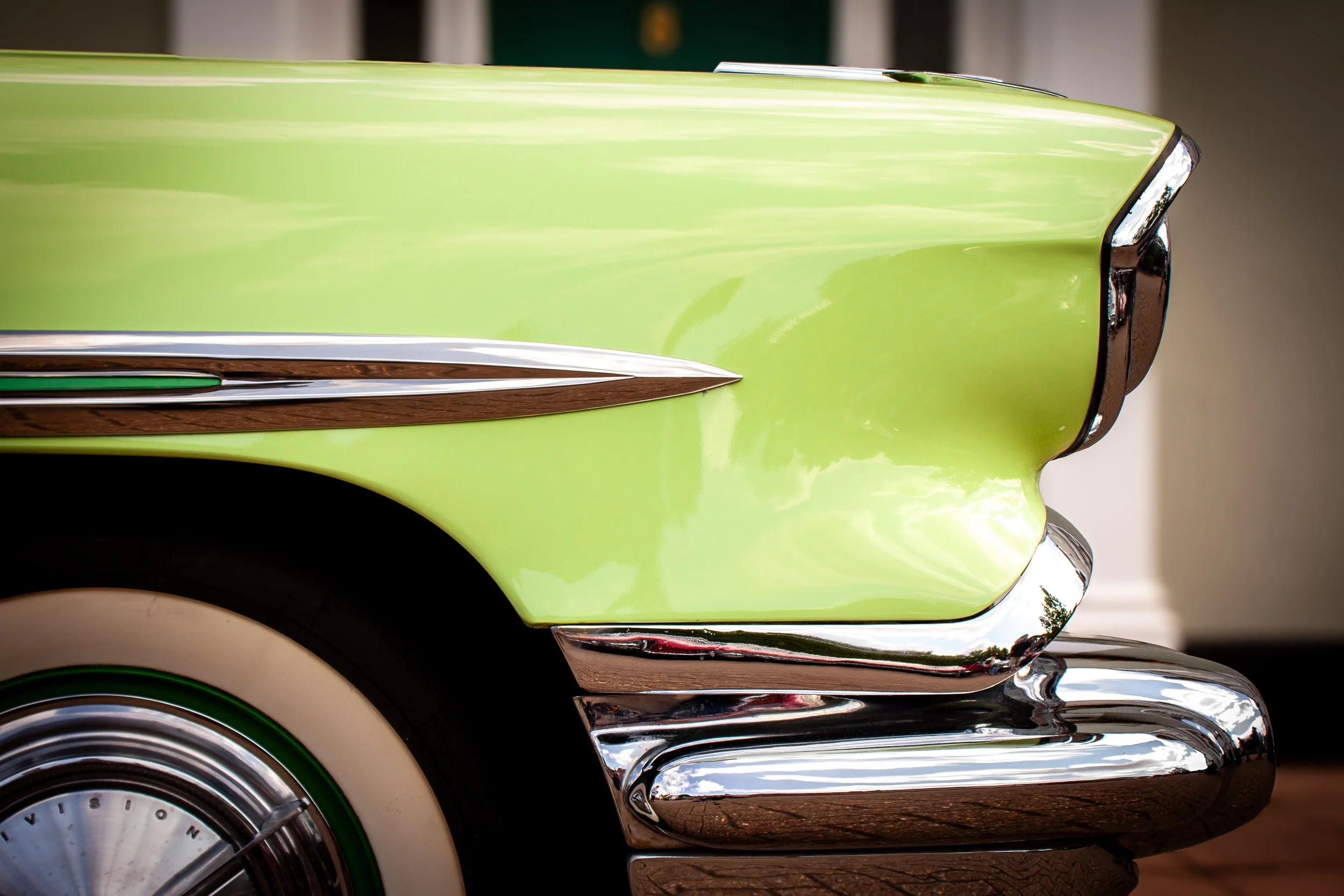 Close-up of a vintage car's front fender and bumper, painted in lime green with chrome detailing, with part of the wheel visible.