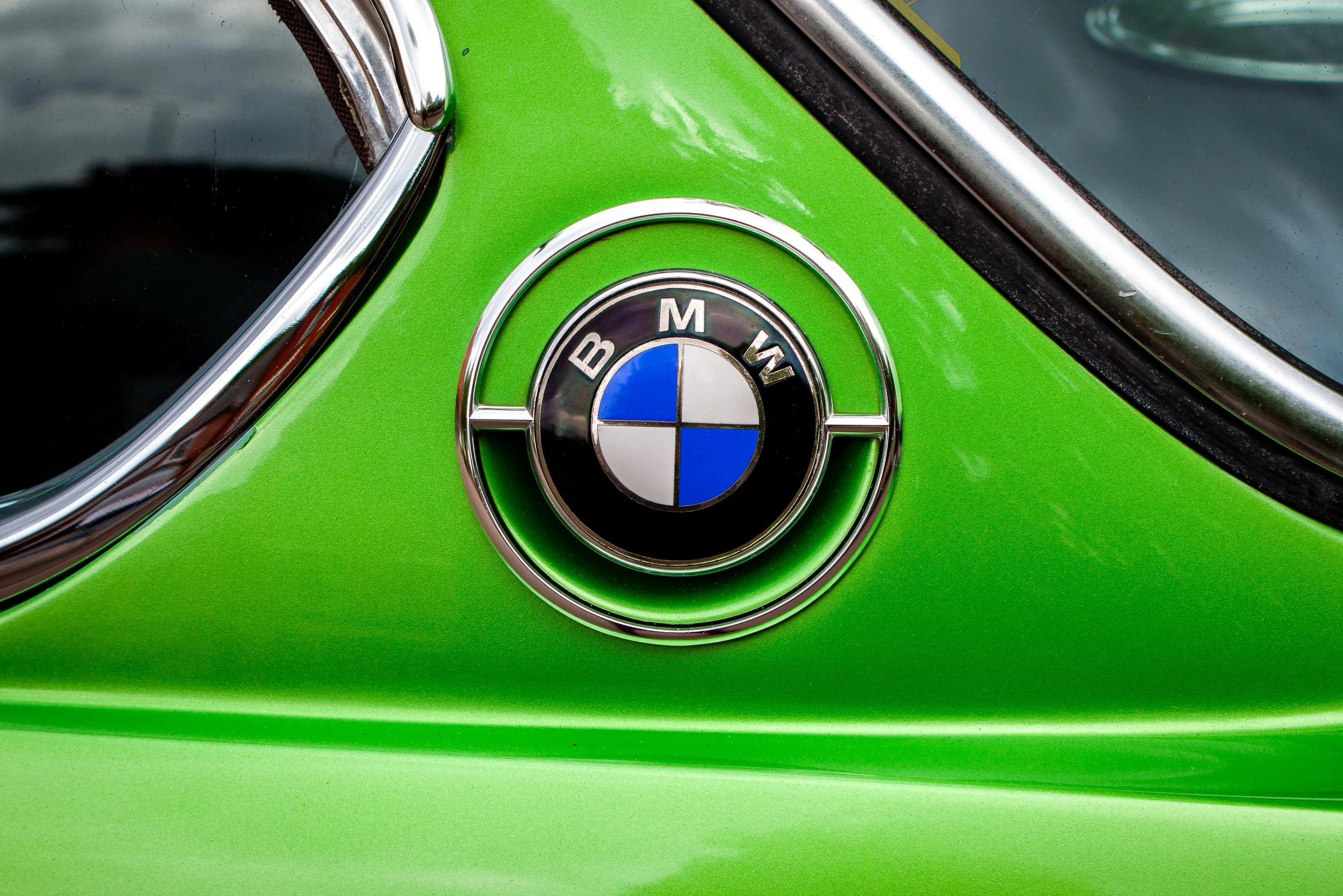 Close-up of a vintage BMW emblem on a bright green car, with part of the windshield and chrome trim visible.